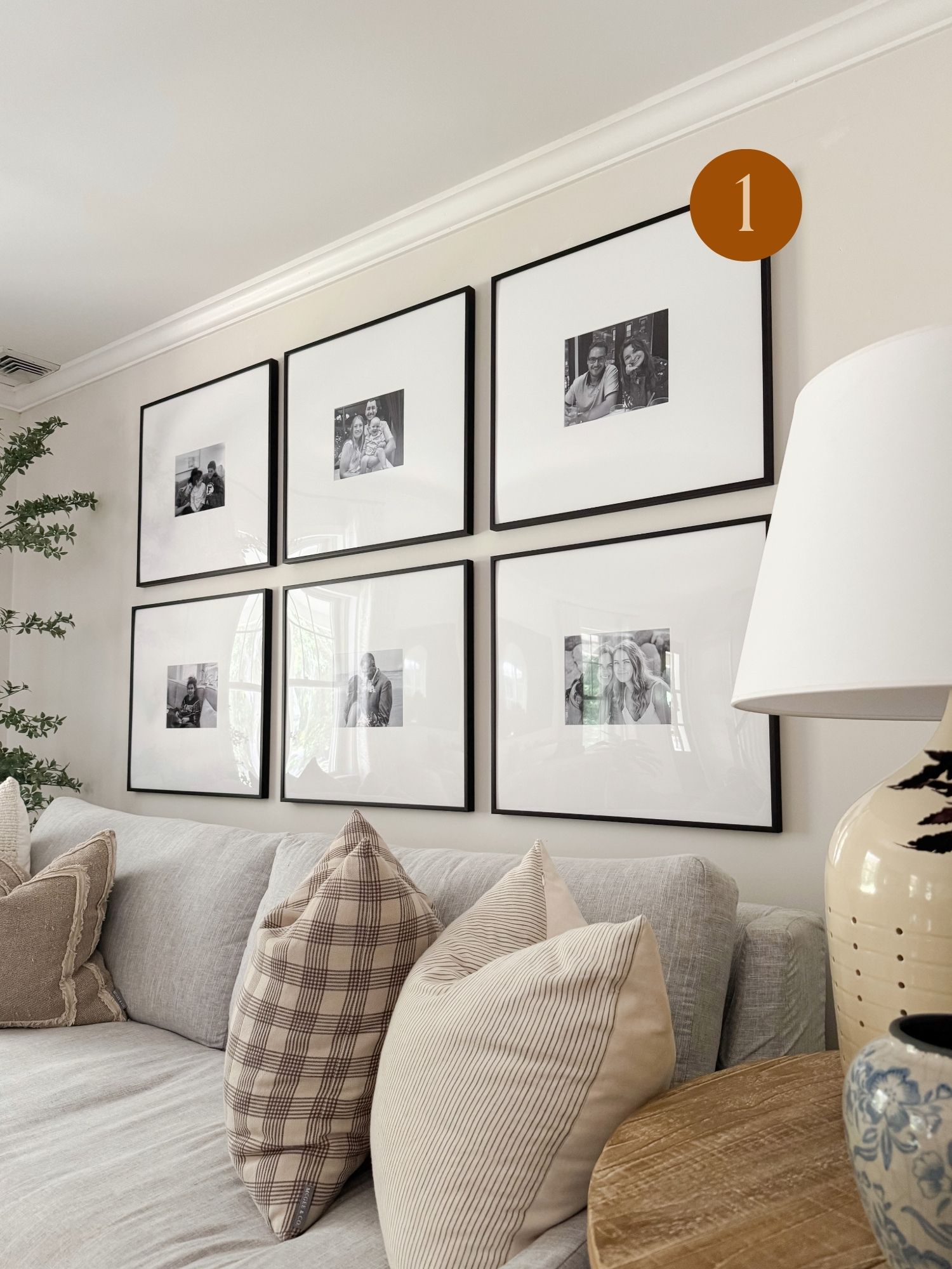 Coastal style living room with a gray sectional sofa, plaid and striped pillows, and a black frame gallery wall of family photos.