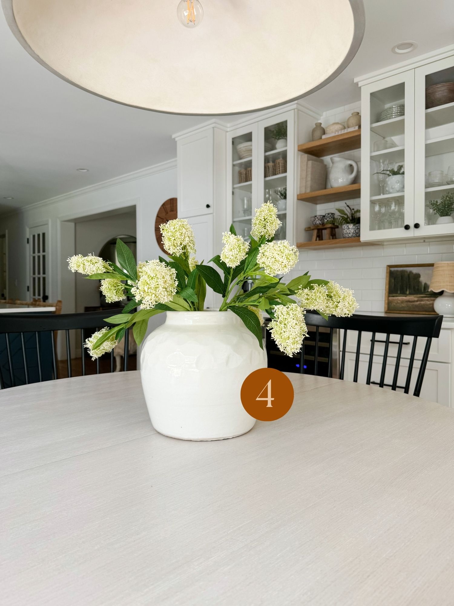 Bright coastal kitchen with a round dining table styled with a white ceramic vase and fresh green floral centerpiece.