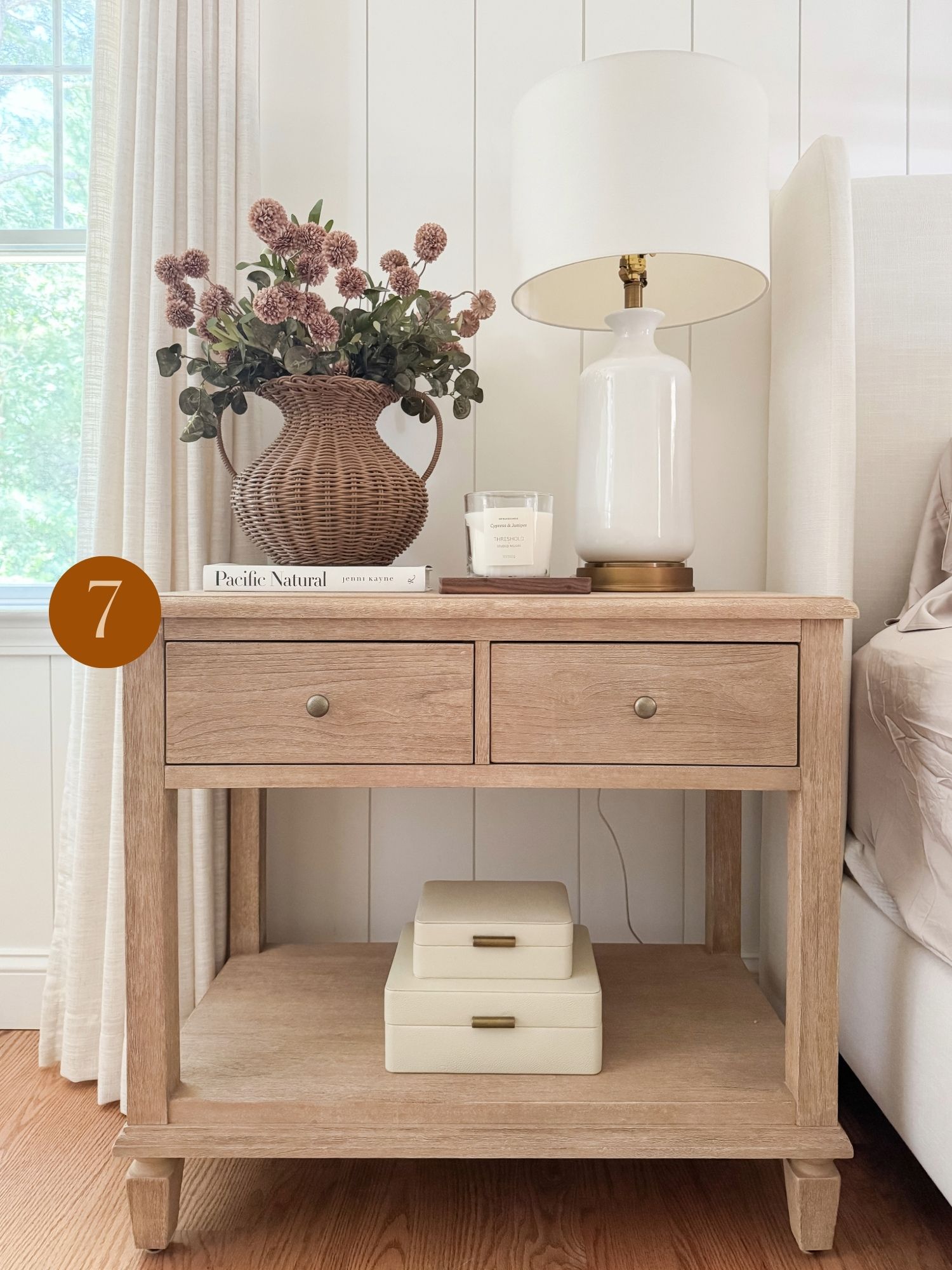 neutral living room styling inspiration Coastal bedroom nightstand with wicker vase arrangement, ceramic lamp, and layered neutral home décor accents.