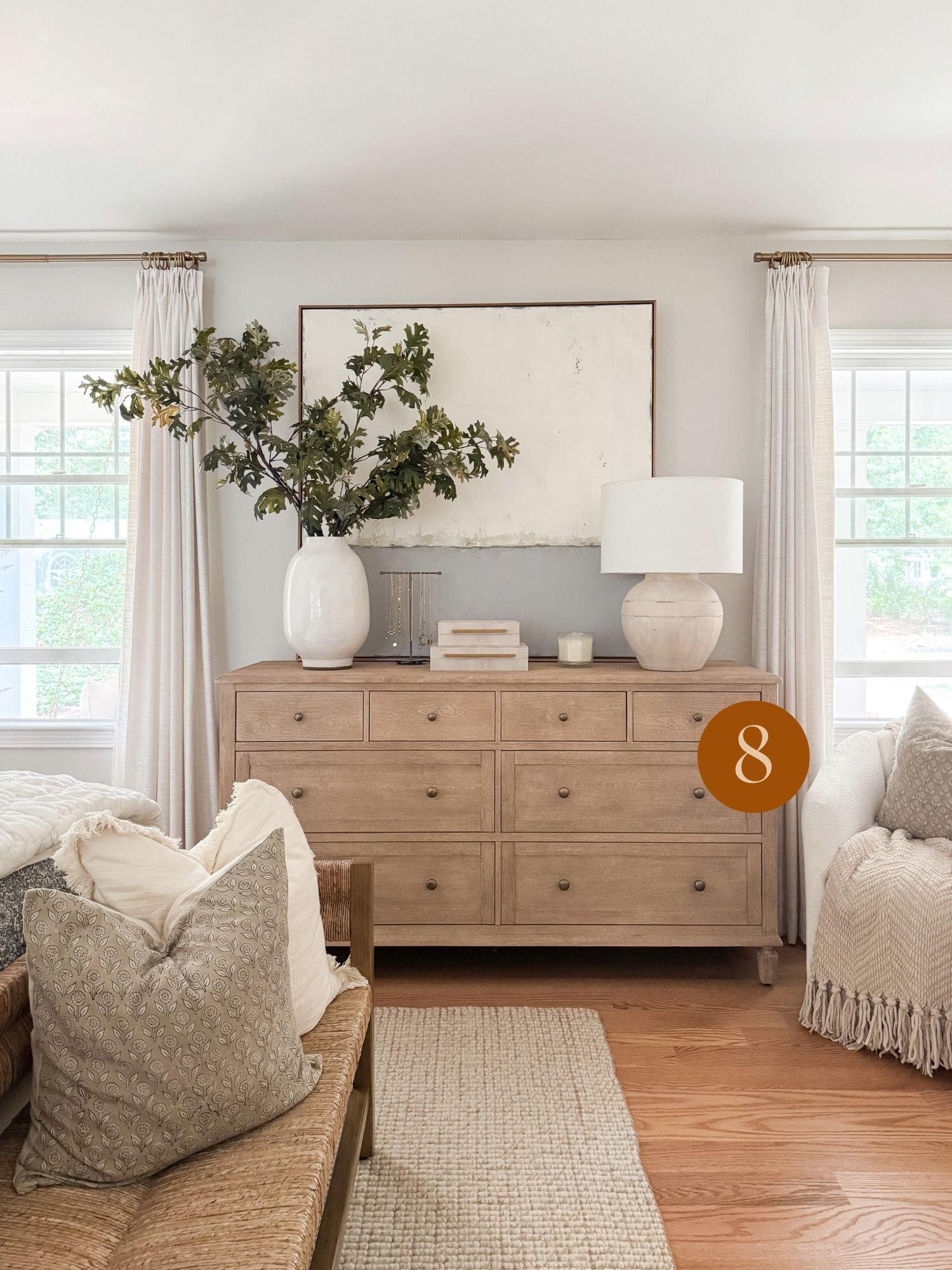 coastal throw pillow inspiration Coastal inspired bedroom with a natural wood dresser, oversized ceramic vases, minimal artwork, and layered neutral textures.
