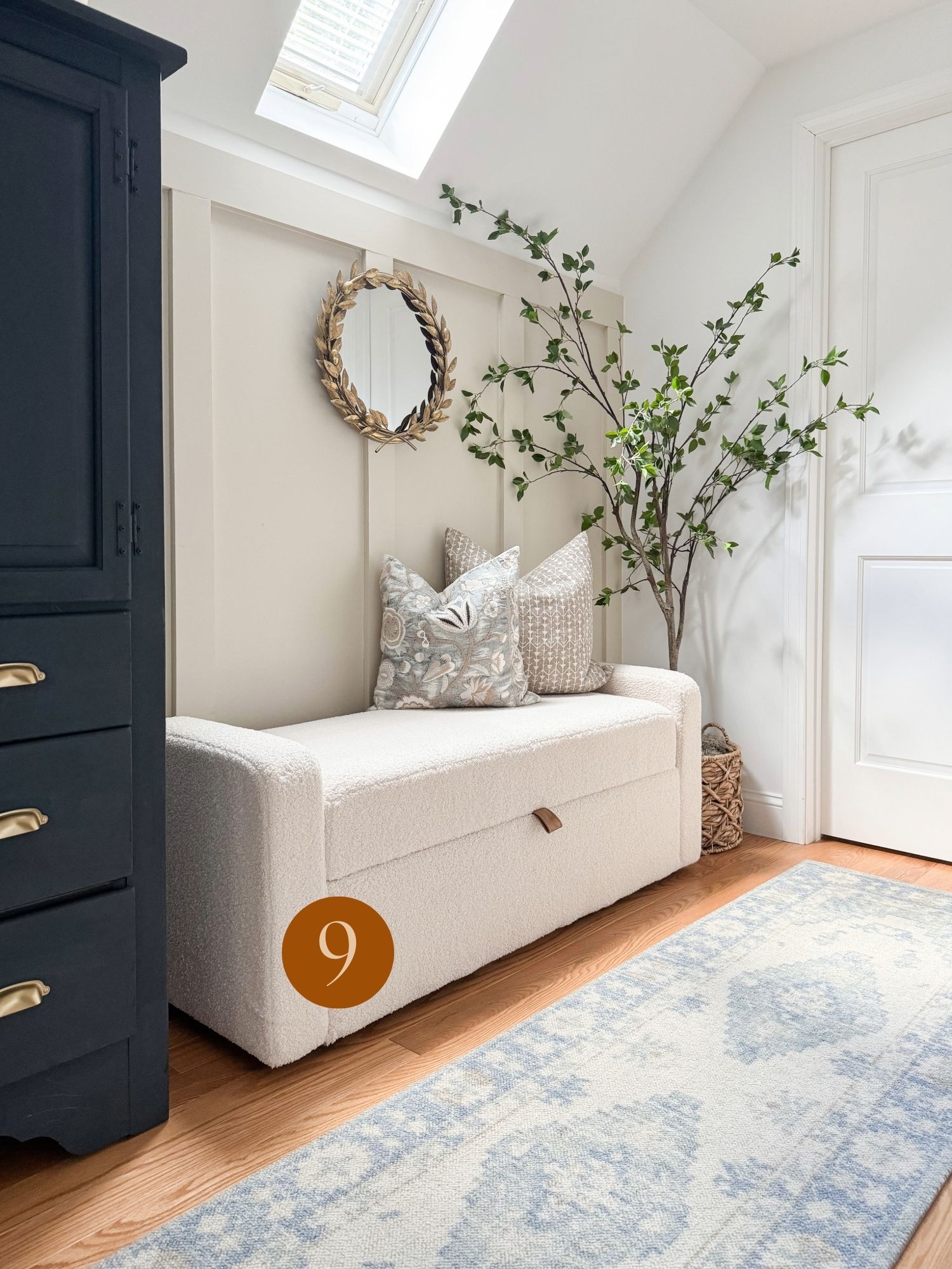neutral living room styling inspiration Coastal farmhouse hallway with a white upholstered storage bench, decorative pillows, gold accent mirror, and blue patterned rug.