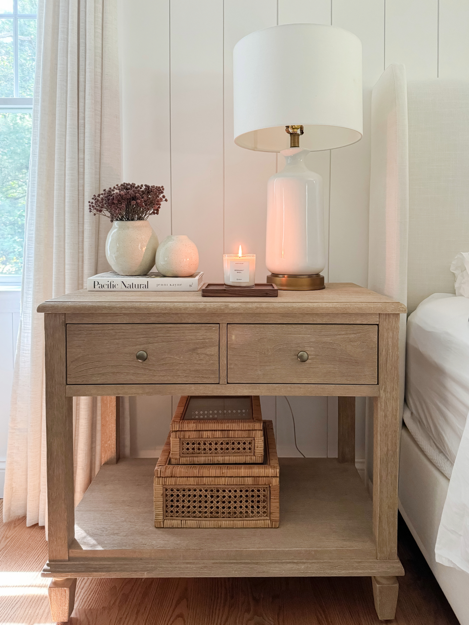 Coastal bedroom nightstand with ceramic table lamp, lit candle, woven baskets, and neutral decor accents. Amazon Prime Day coastal home finds.