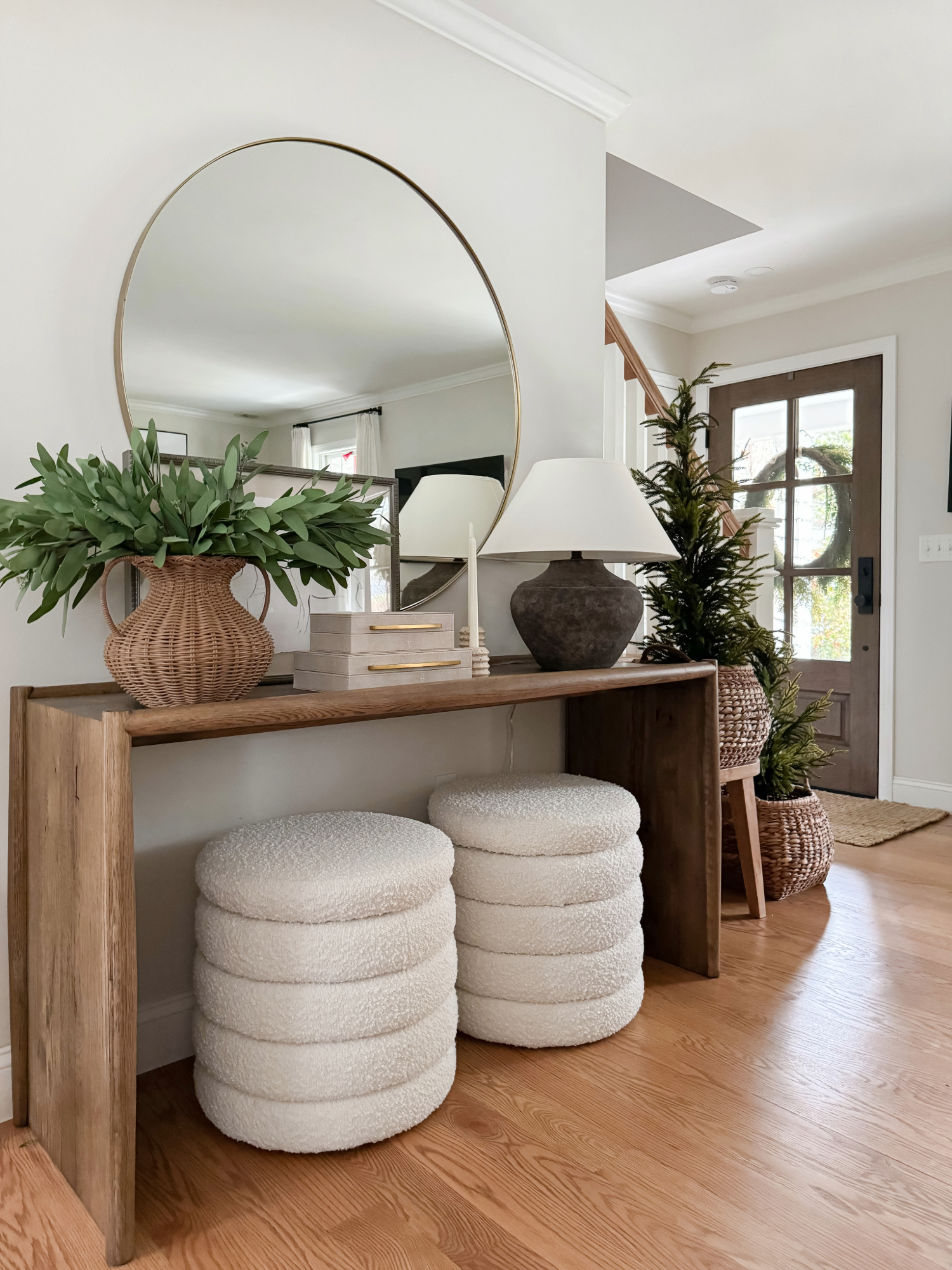 Coastal inspired entryway with a round gold mirror, rustic wood console table, woven basket vase with greenery, ceramic lamp, and boucle ottomans. Neutral coastal home decor finds for Amazon Prime Day.