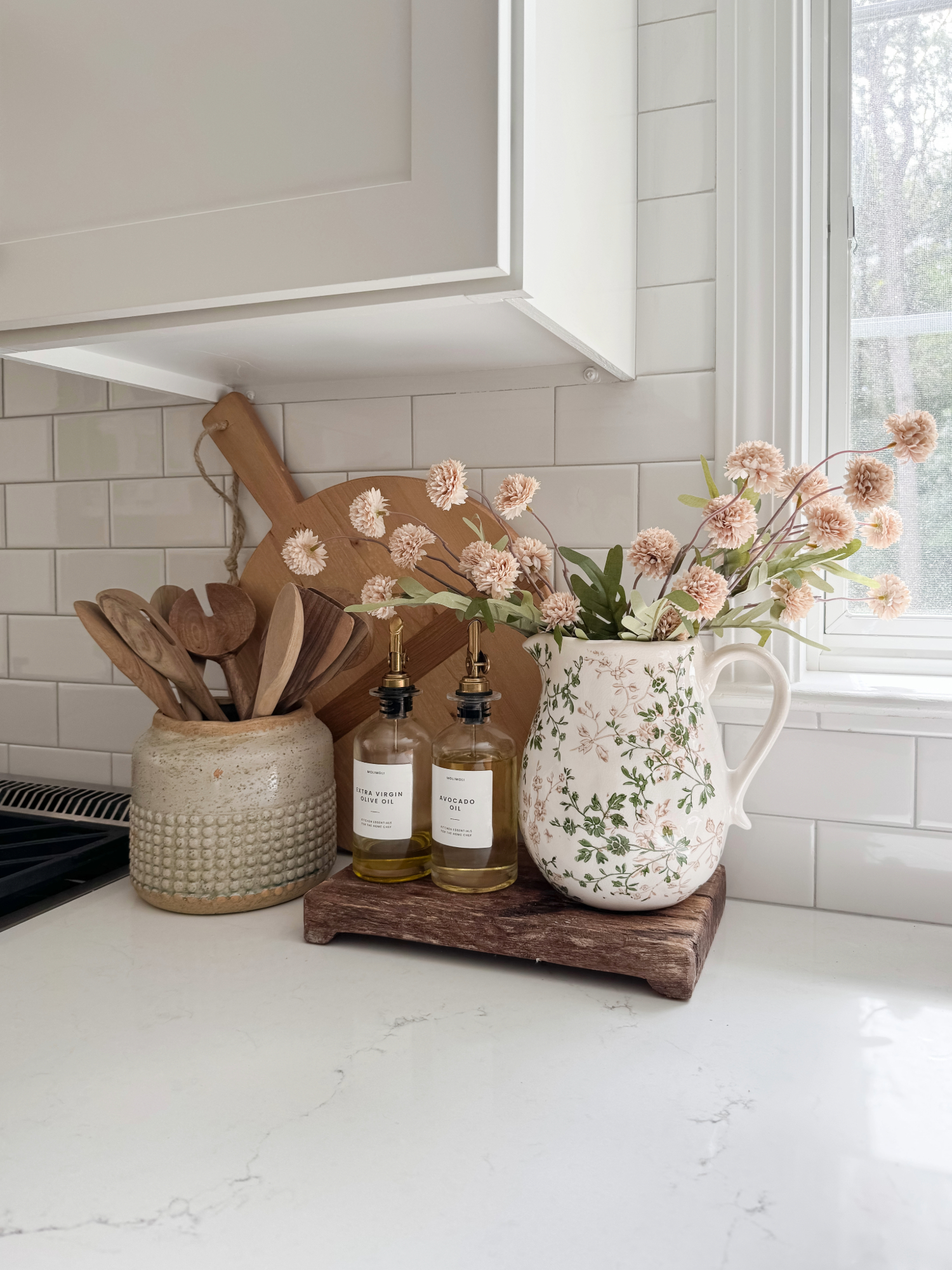 Coastal farmhouse kitchen with white subway tile backsplash, ceramic utensil crock, floral pitcher, cutting boards, and glass oil bottles. Neutral Amazon Prime Day kitchen finds.