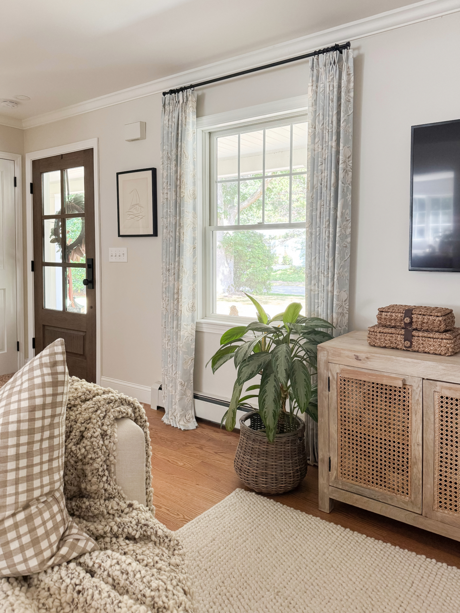Coastal living room with woven rattan cabinet, blue floral curtains, potted plant in wicker basket, and cozy throw blanket. Amazon Prime Day home decor deals.