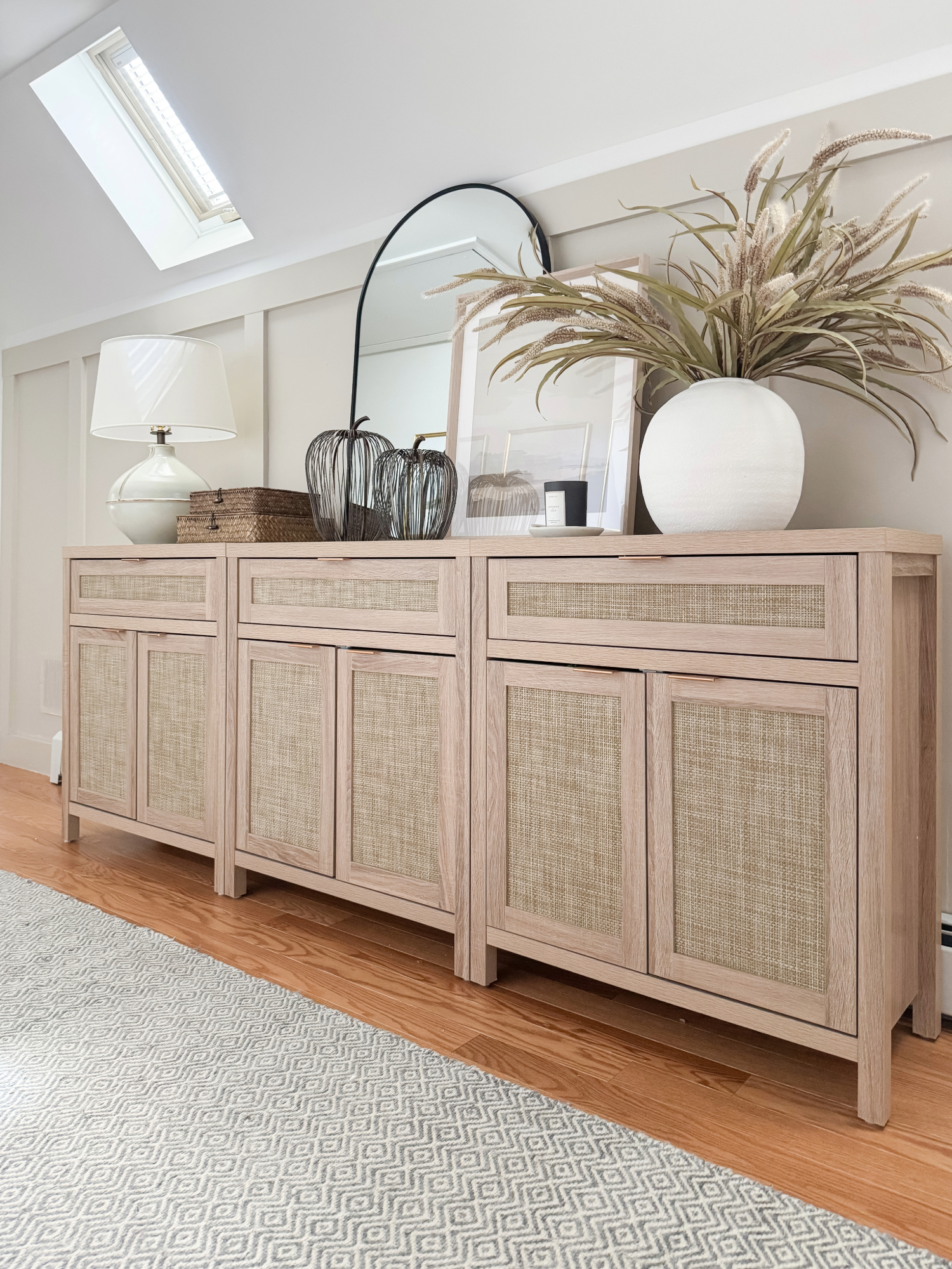 Coastal console table with woven-front cabinets, round mirror, ceramic vase with greenery, table lamp, and neutral styling. Modern coastal Amazon Prime Day finds.
