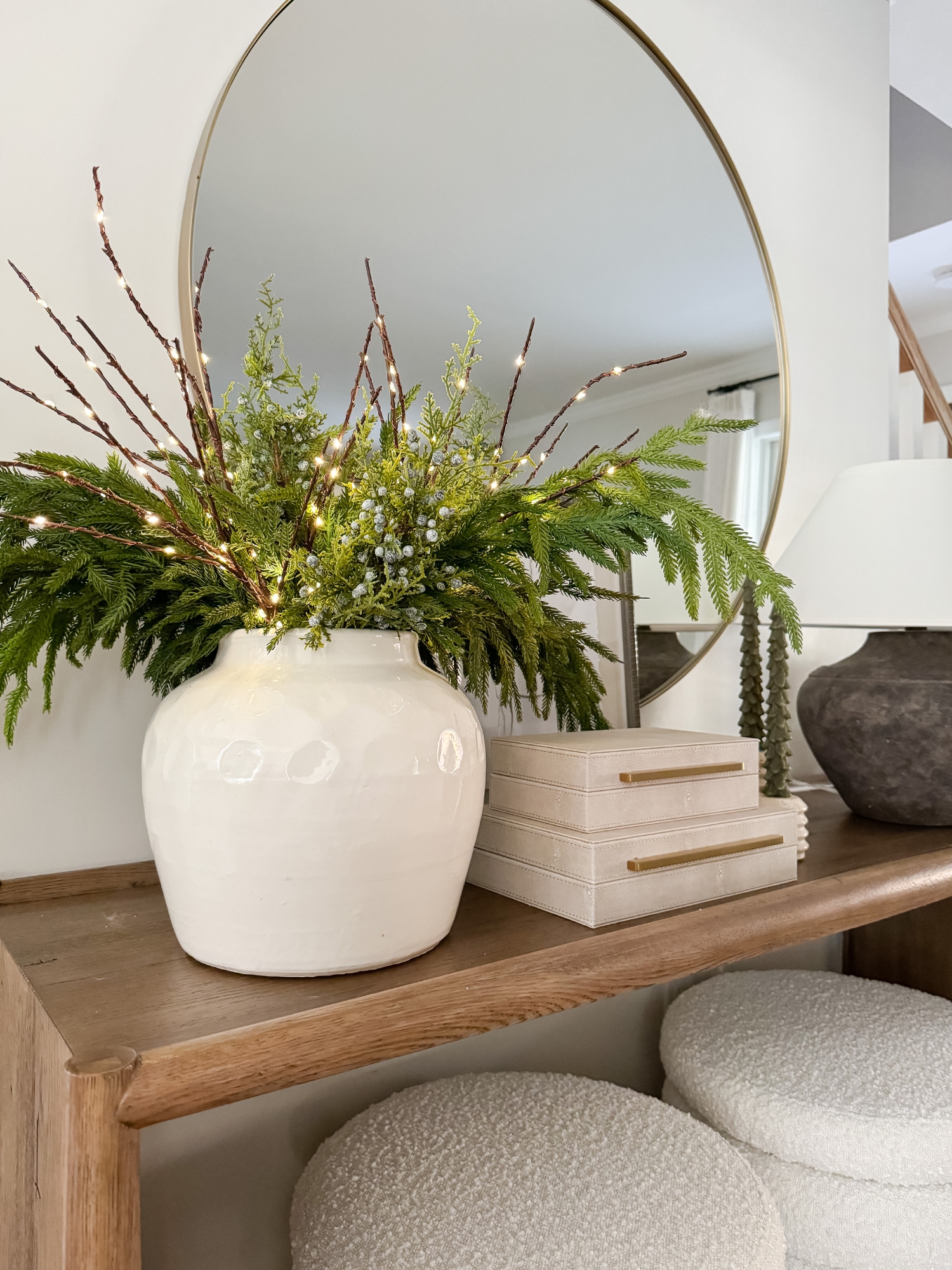 Console table styled with natural greenery in a white vase, warm twinkle lights, and simple holiday accents for a minimal Christmas look.