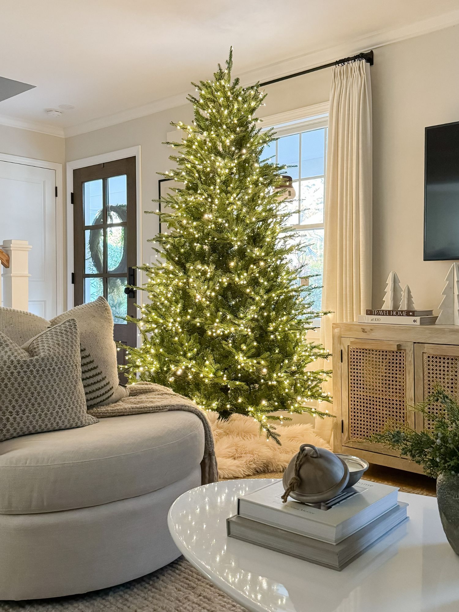 Softly lit living room featuring a Christmas tree, layered neutrals, and warm tones that create a relaxed, inviting holiday feel.