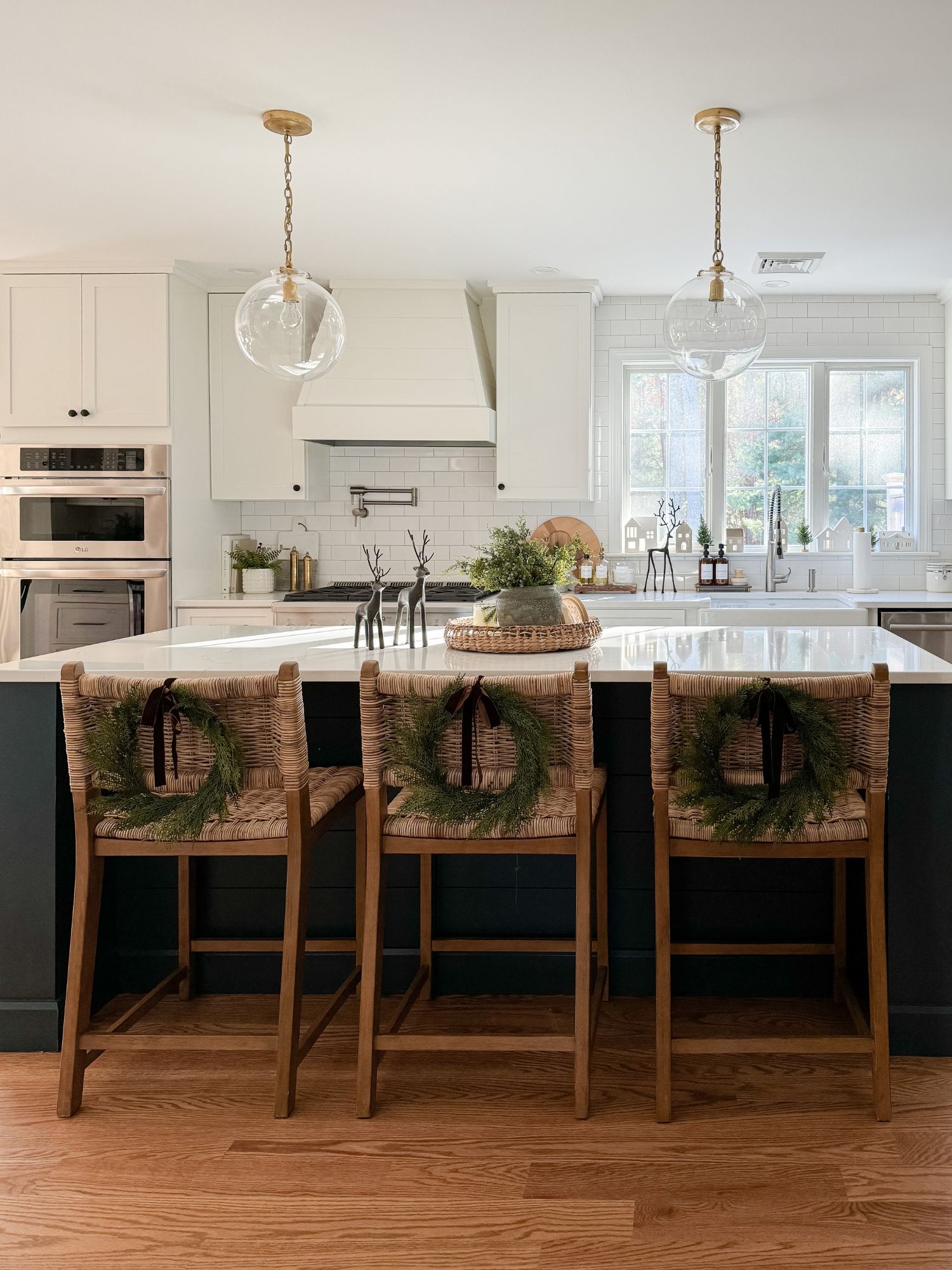 Kitchen decorated for Christmas with small wreaths on barstools, greenery, and neutral finishes for a simple festive update.