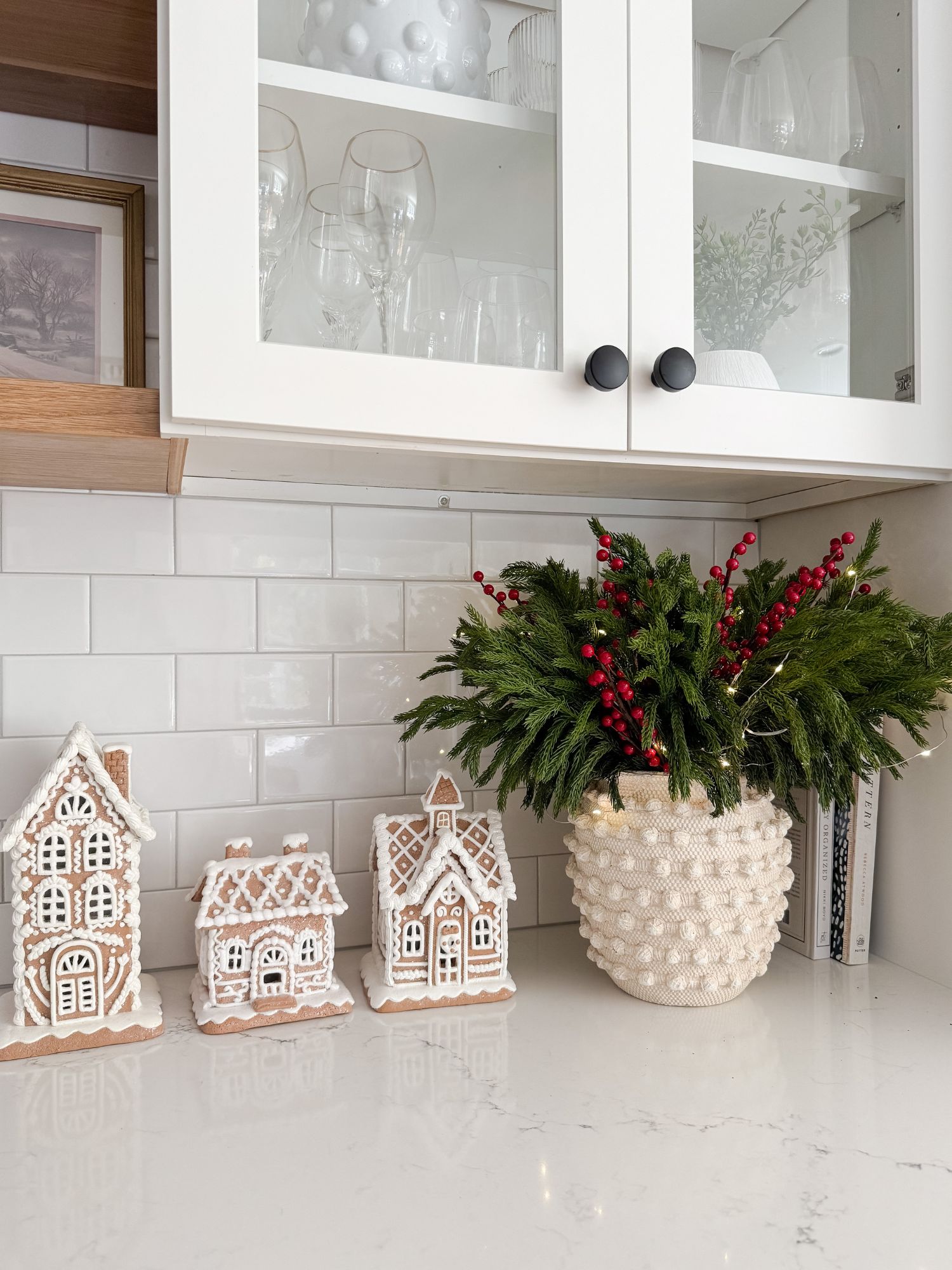 Christmas kitchen counter styled with gingerbread houses, greenery with berries, and soft lighting for a nostalgic holiday touch.