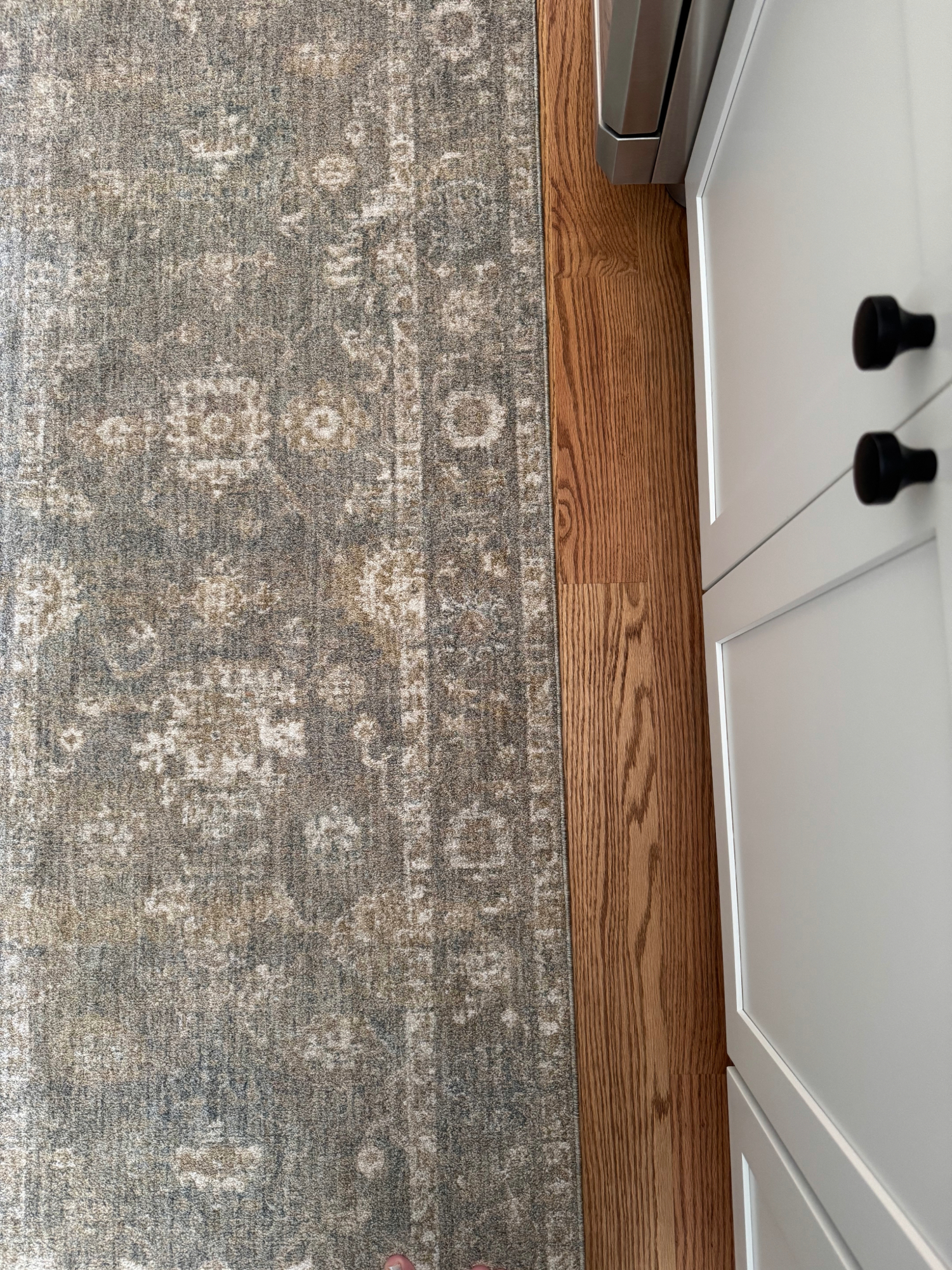 Muted vintage-style kitchen runner with neutral pattern and soft texture against hardwood floors for a cozy kitchen flooring detail.