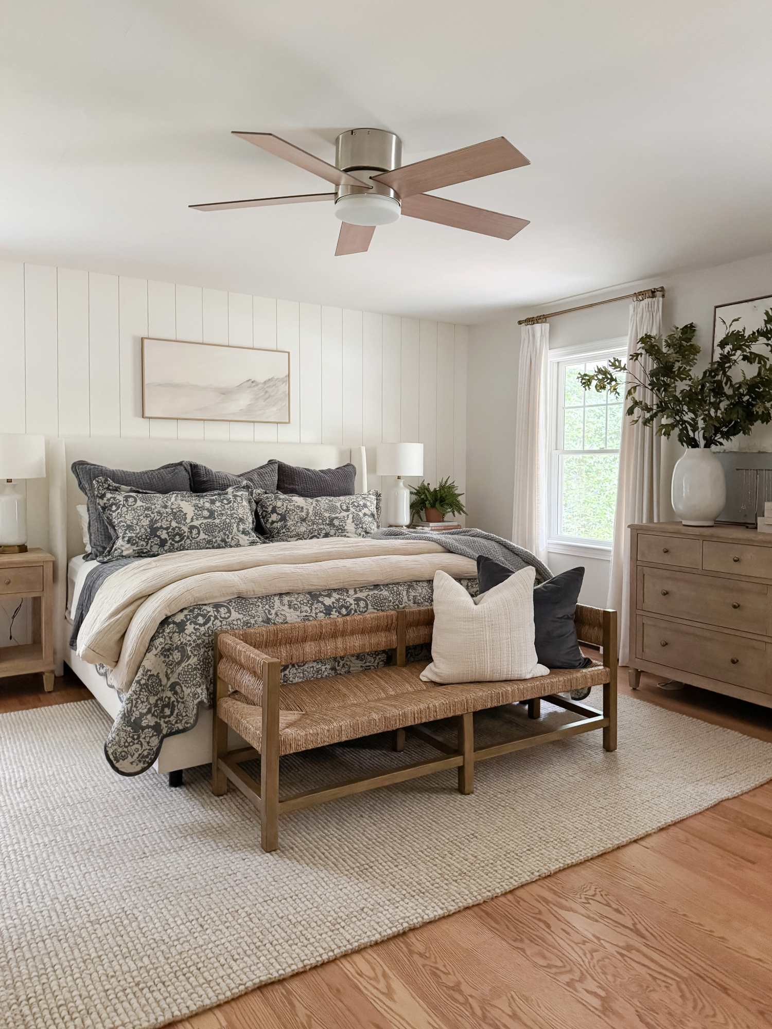 Neutral bedroom design with layered quilts, woven bench, and natural wood furniture for a calm and cozy fall and winter home aesthetic.