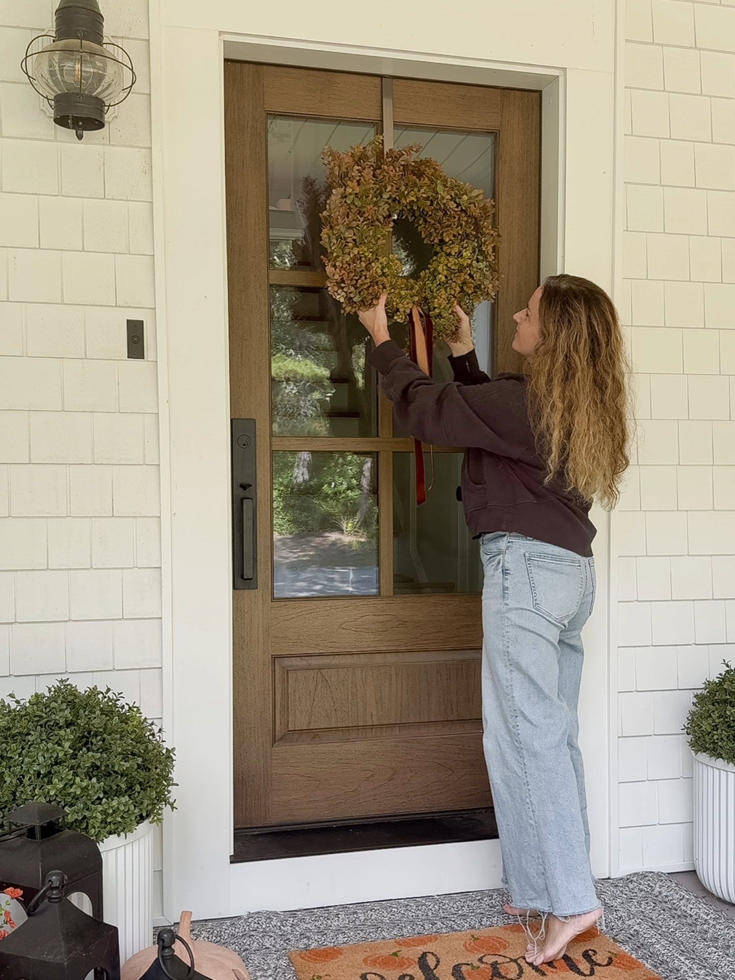 Coastal farmhouse front porch with natural wood door, seasonal wreath, potted greenery, and lanterns. Amazon Prime Day outdoor home decor finds.