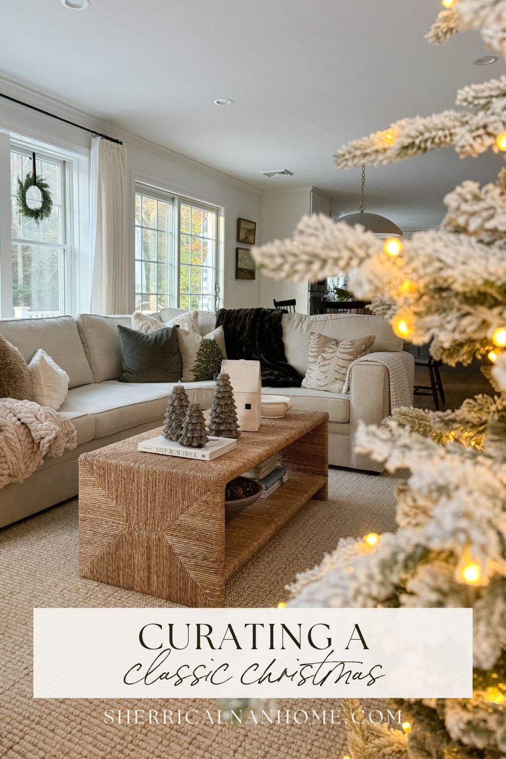 Neutral living room decorated for Christmas with a cozy sectional, textured coffee table, soft throw blankets, and a glowing tree in the foreground.