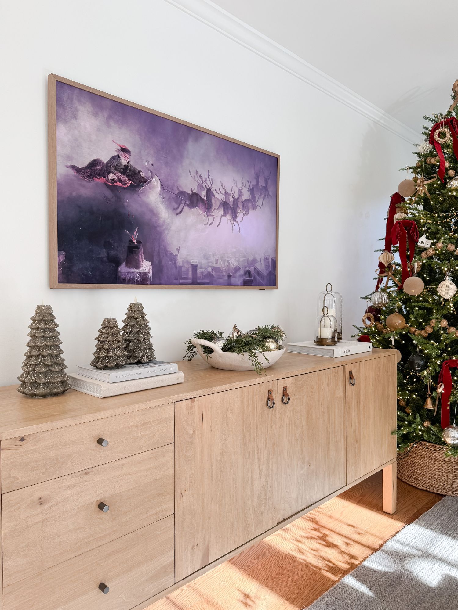 Family room sideboard decorated with Christmas trees, greenery, and a serving bowl, with a Samsung Frame TV above and a decorated Christmas tree nearby.