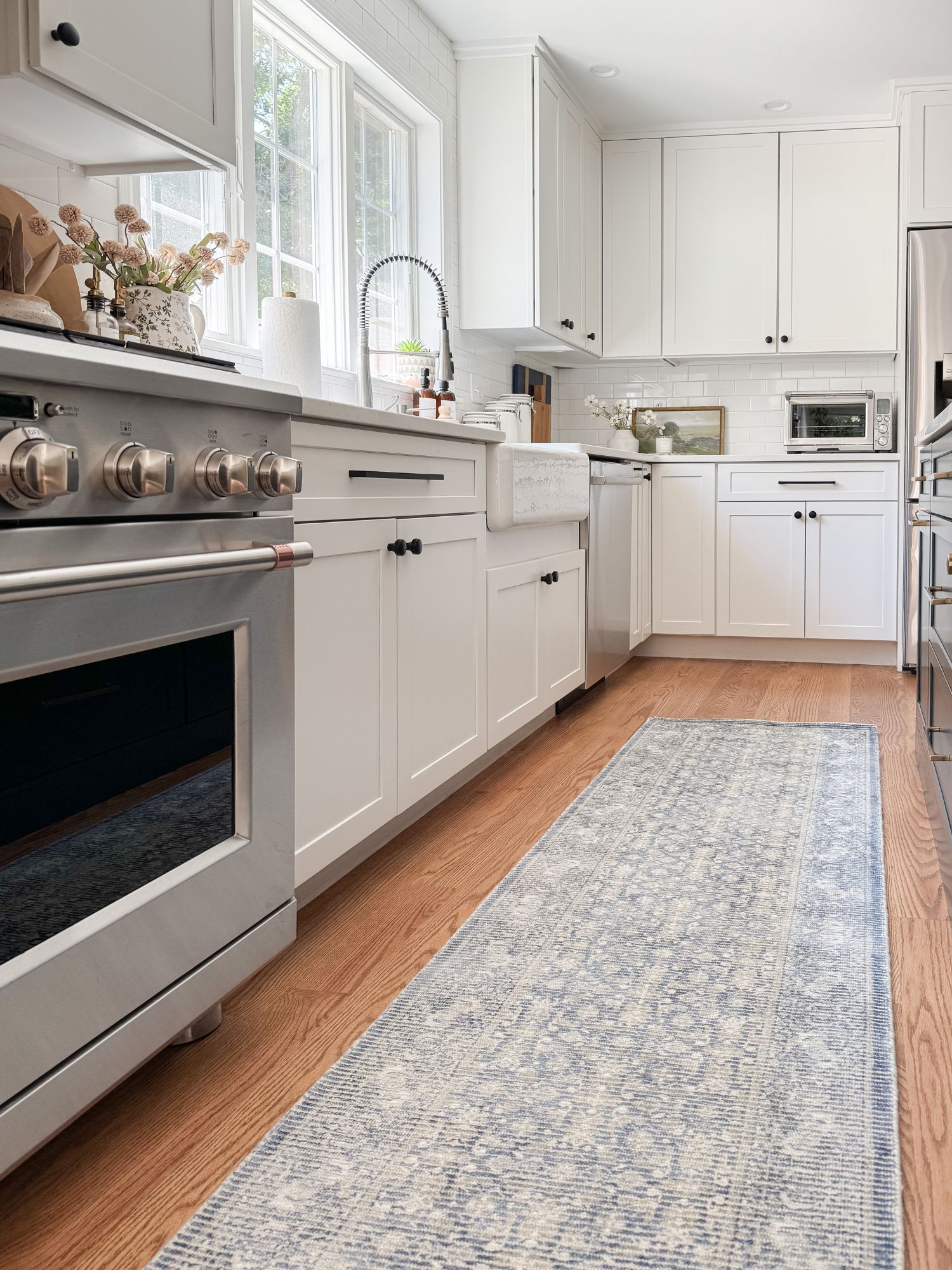 Bright coastal kitchen with white cabinets, wood floors, and a soft blue patterned runner rug adding warmth and texture