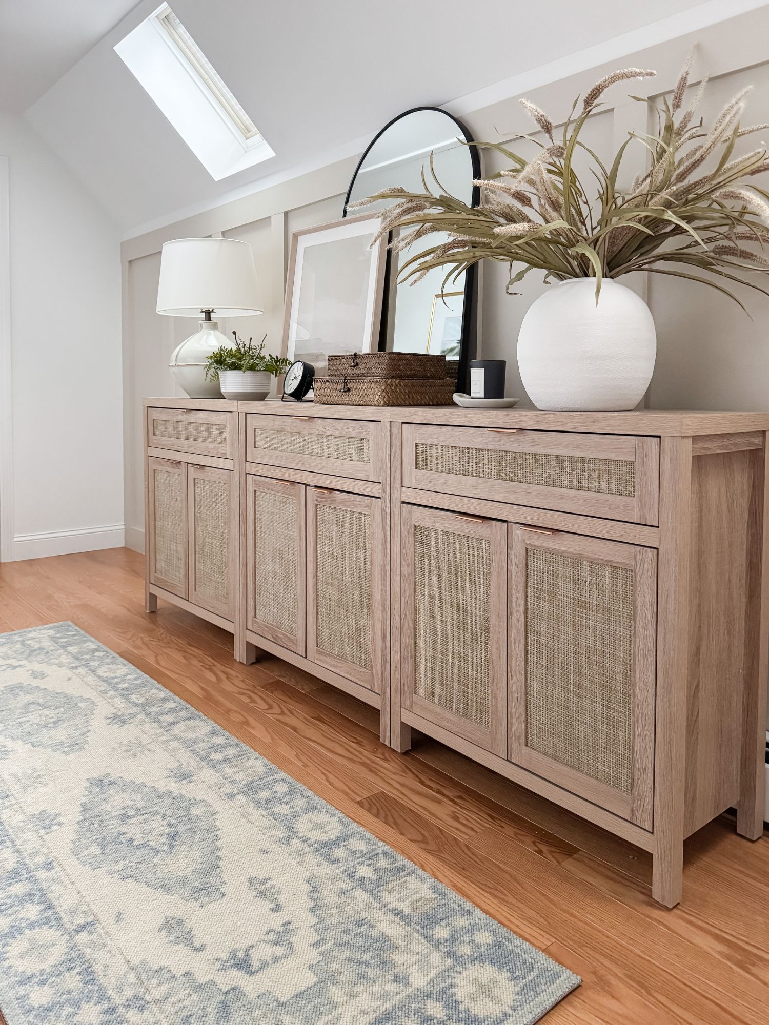Coastal home storage area with a woven front sideboard buffet styled with decor, lamp, mirror, and neutral rug
