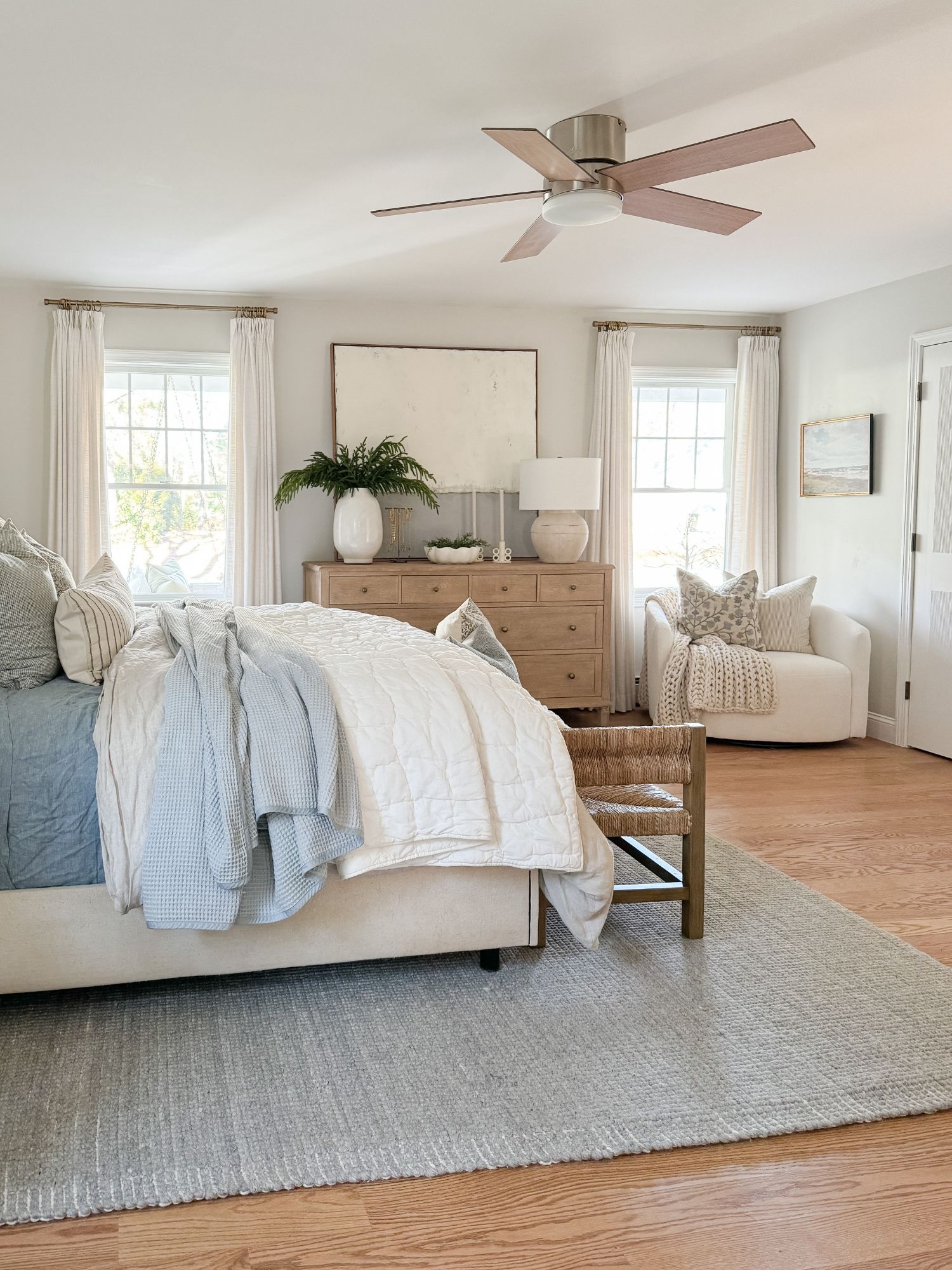 Winter bedroom styled in whites and soft blues with layered pillows, quilted bedding, and calm coastal tones.