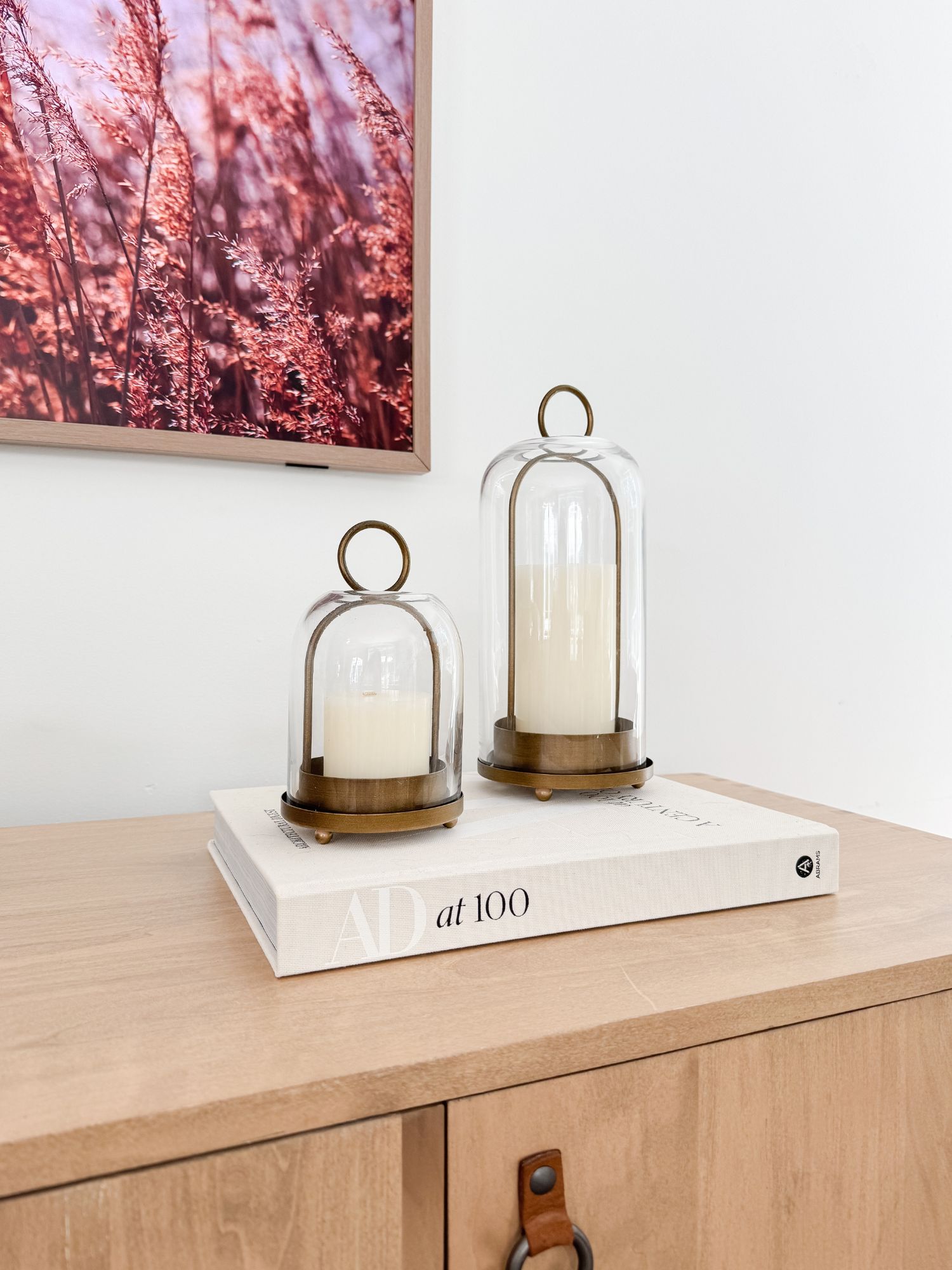 Neutral console styled with glass and metal candle holders placed on a coffee table book for a coastal vignette