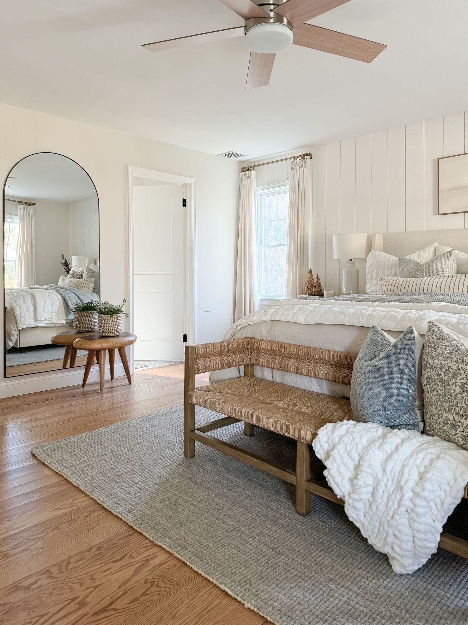 Winter bedroom with arched mirror, woven bench, chunky knit throw, and light neutral coastal textures.