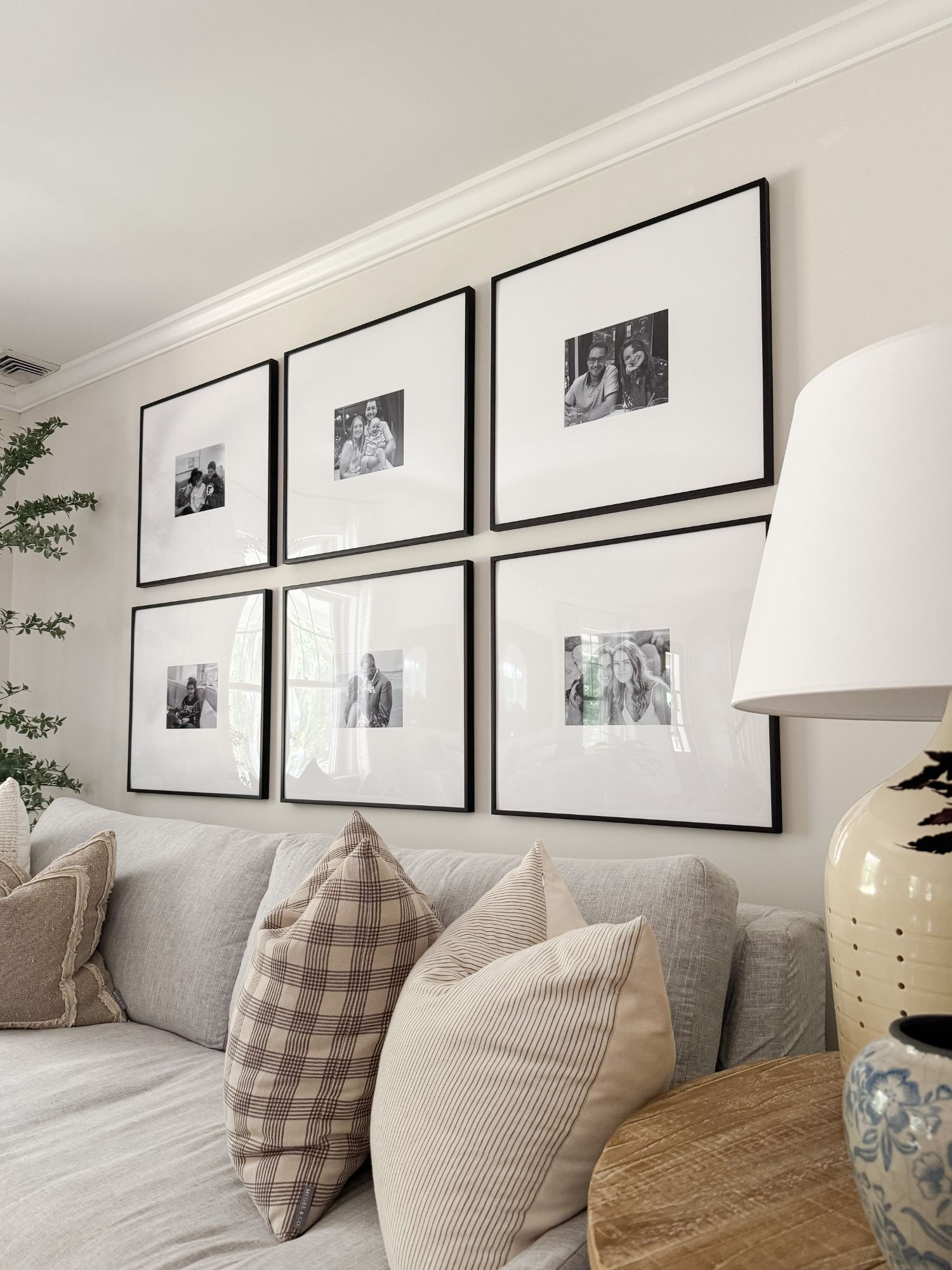Coastal living room with light sofa, neutral throw pillows, and a wood frame gallery wall featuring black and white family photos