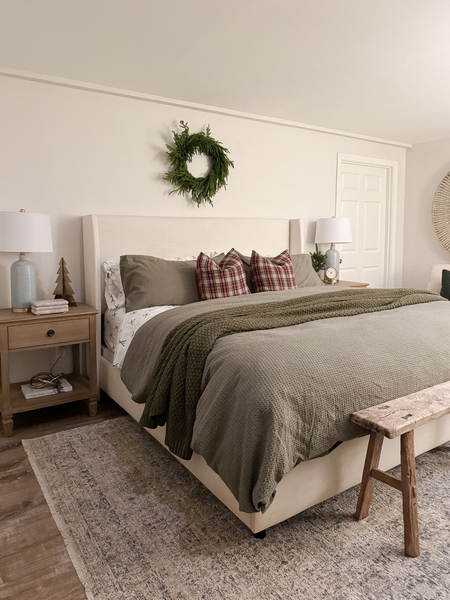 Guest winter bedroom styled for the holidays with olive green quilt, plaid pillows, and simple wreath above the headboard.