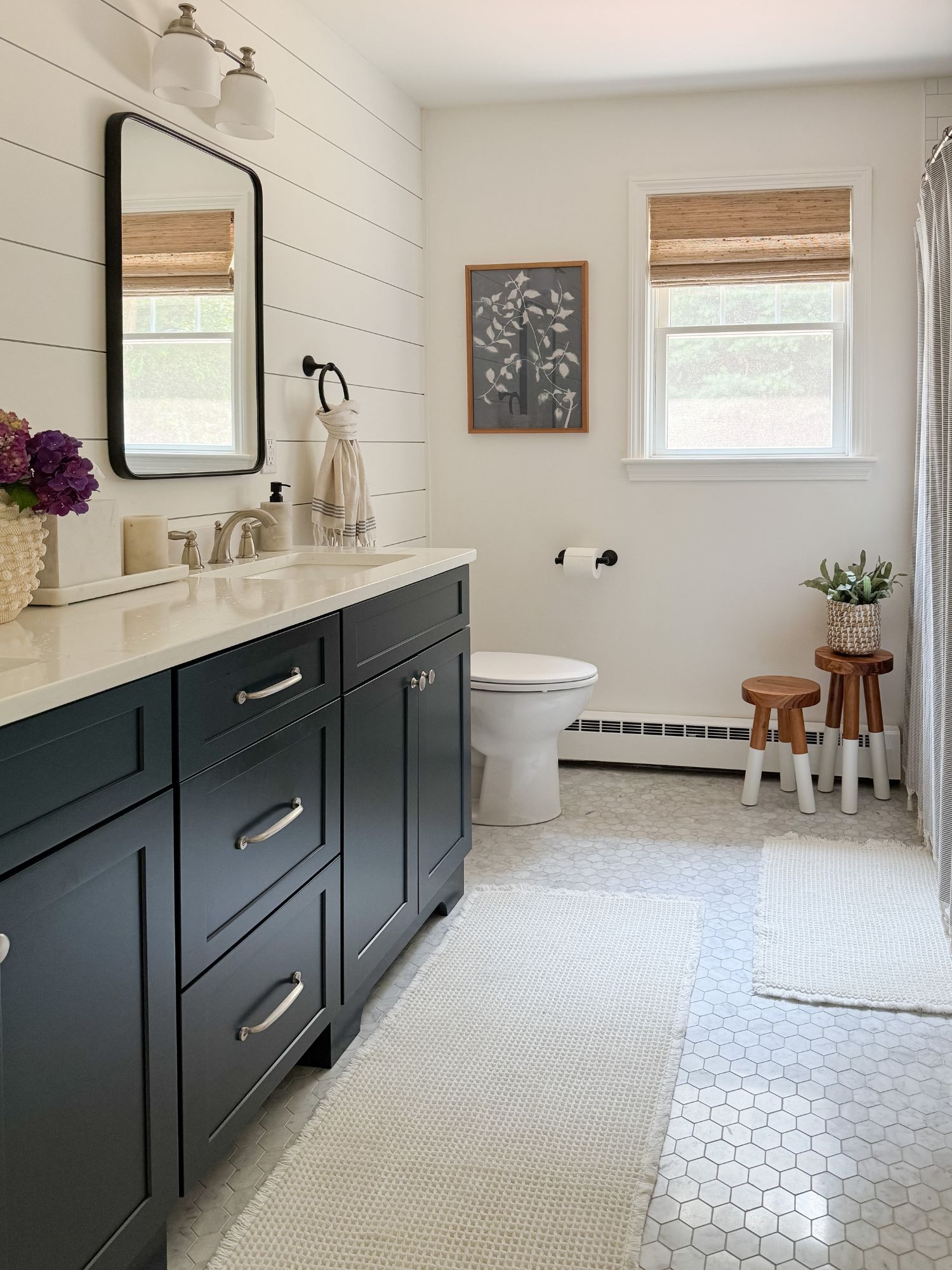 Coastal bathroom with navy vanity, white shiplap walls, hex tile flooring, and neutral waffle bath mats