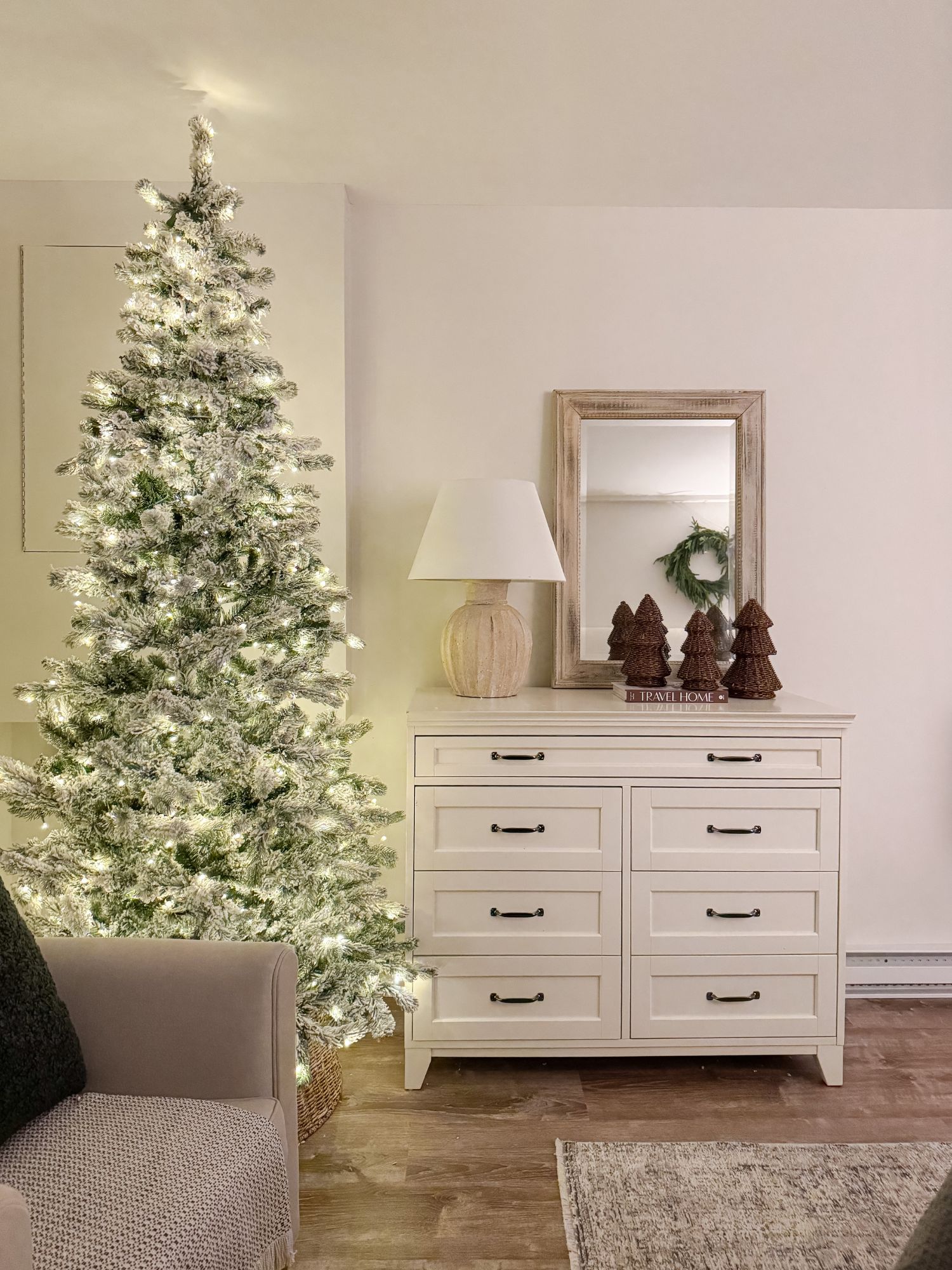 Guest winter bedroom with flocked Christmas tree, white dresser, layered mirror, and neutral holiday accents.