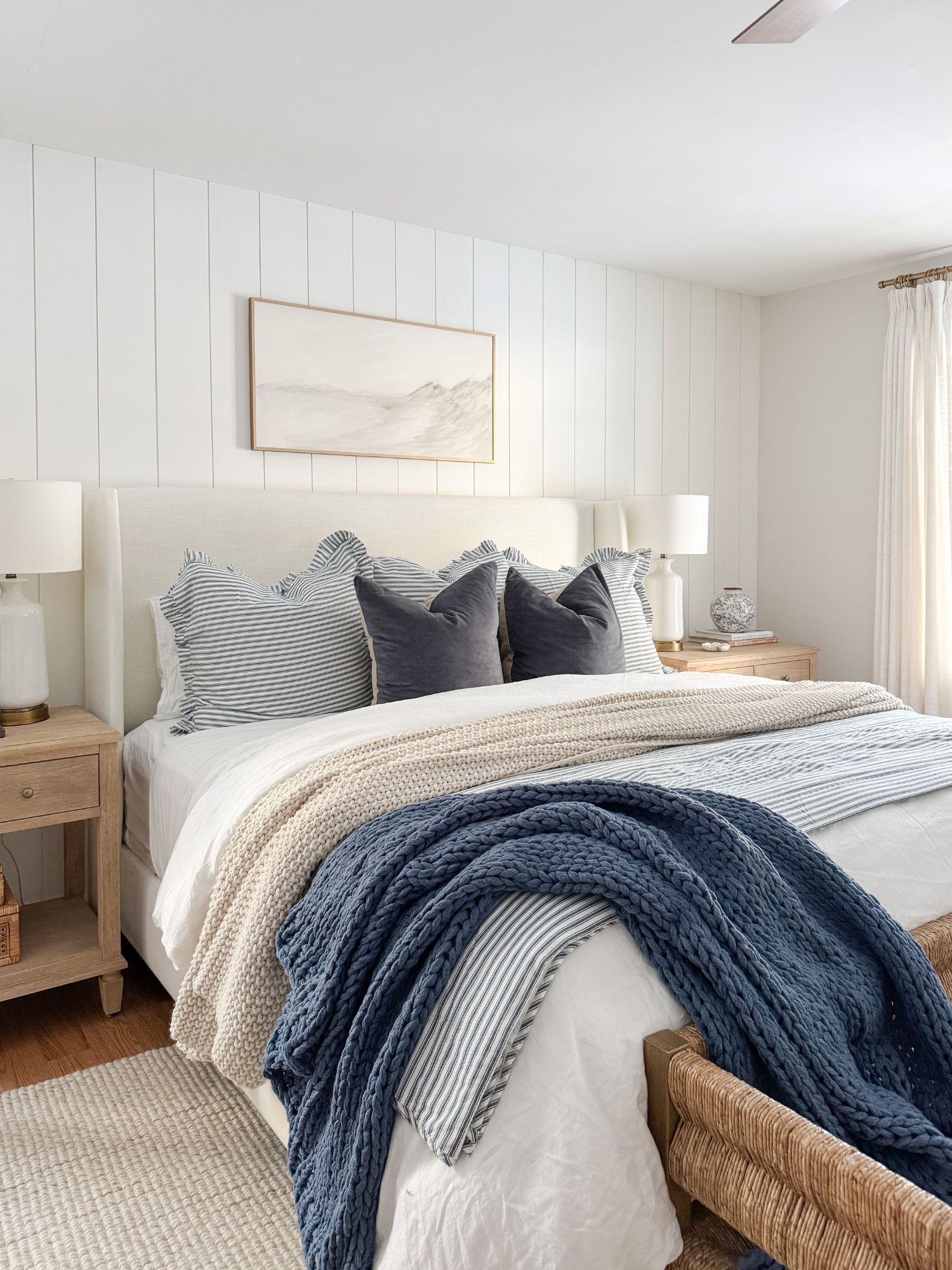 Cape Cod inspired bedroom featuring winter white bedding, light blue duvet cover, textured knit blanket, and soft neutral nightstand styling.
