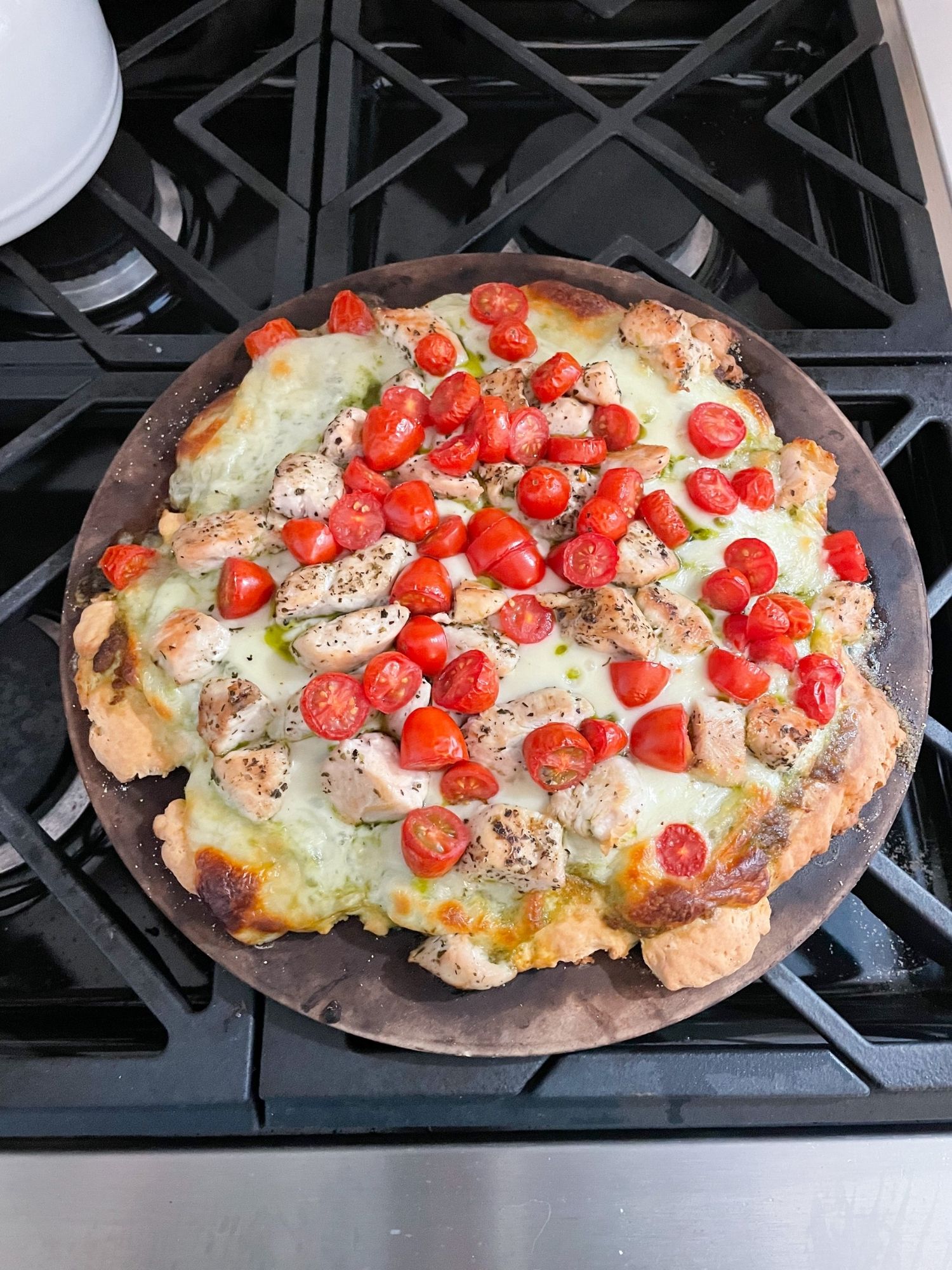 Homemade chicken pesto pizza with melted mozzarella, cherry tomatoes, and golden crust on a baking stone for an easy cozy weeknight dinner at home.