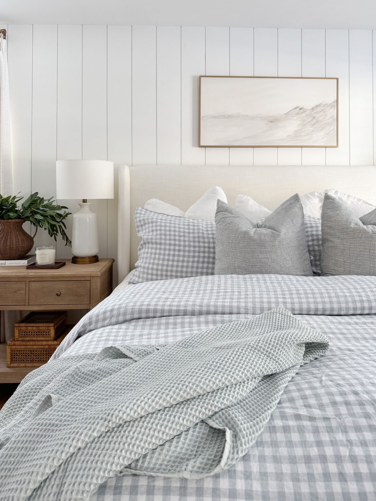Cape Cod bedroom with a white upholstered bed, chunky blue knit blanket, striped pillows, and winter white bedding for a cozy coastal look.