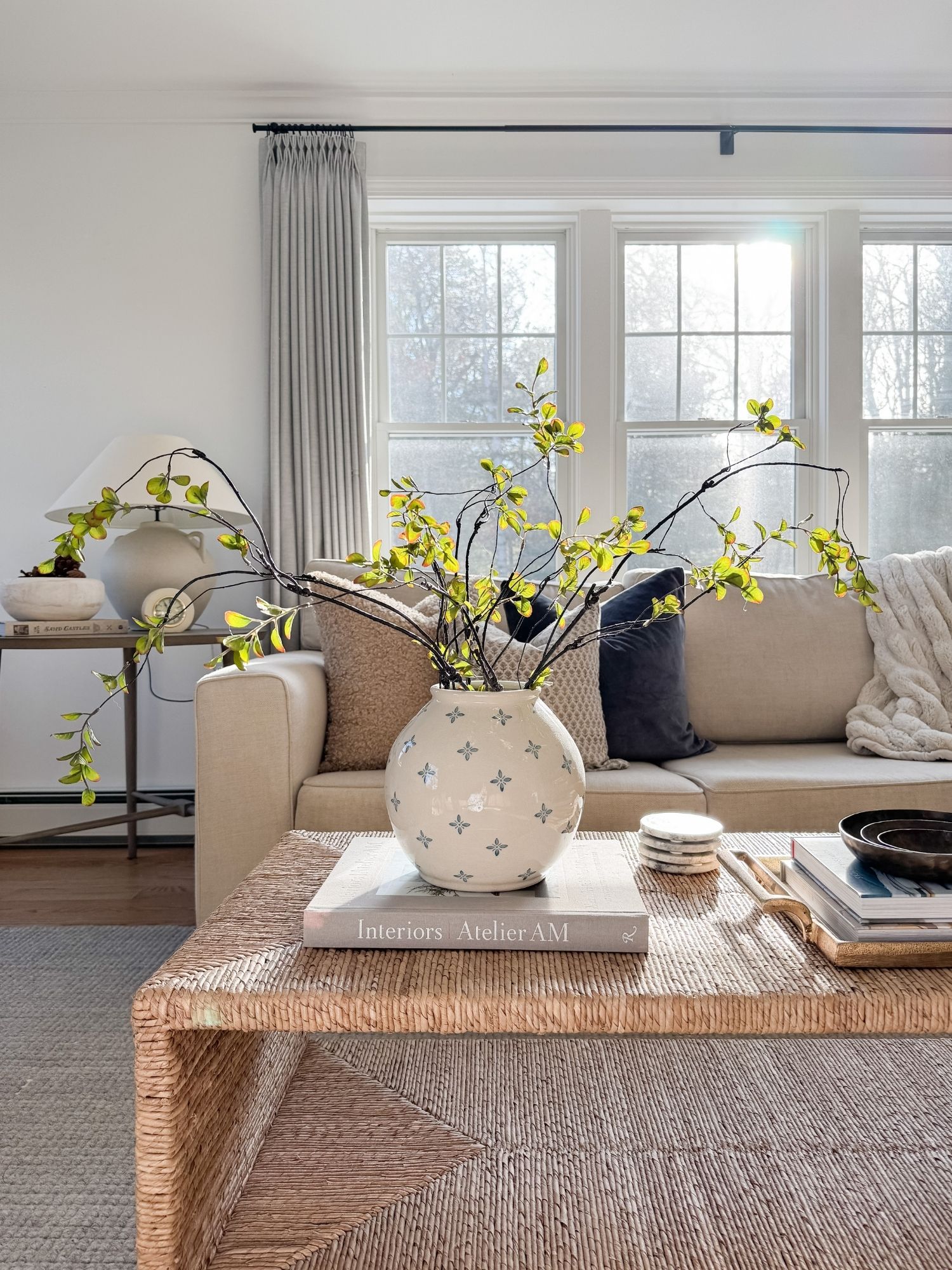 Neutral living room coffee table with woven texture, ceramic vase, greenery, and layered decor in a cozy family friendly home.