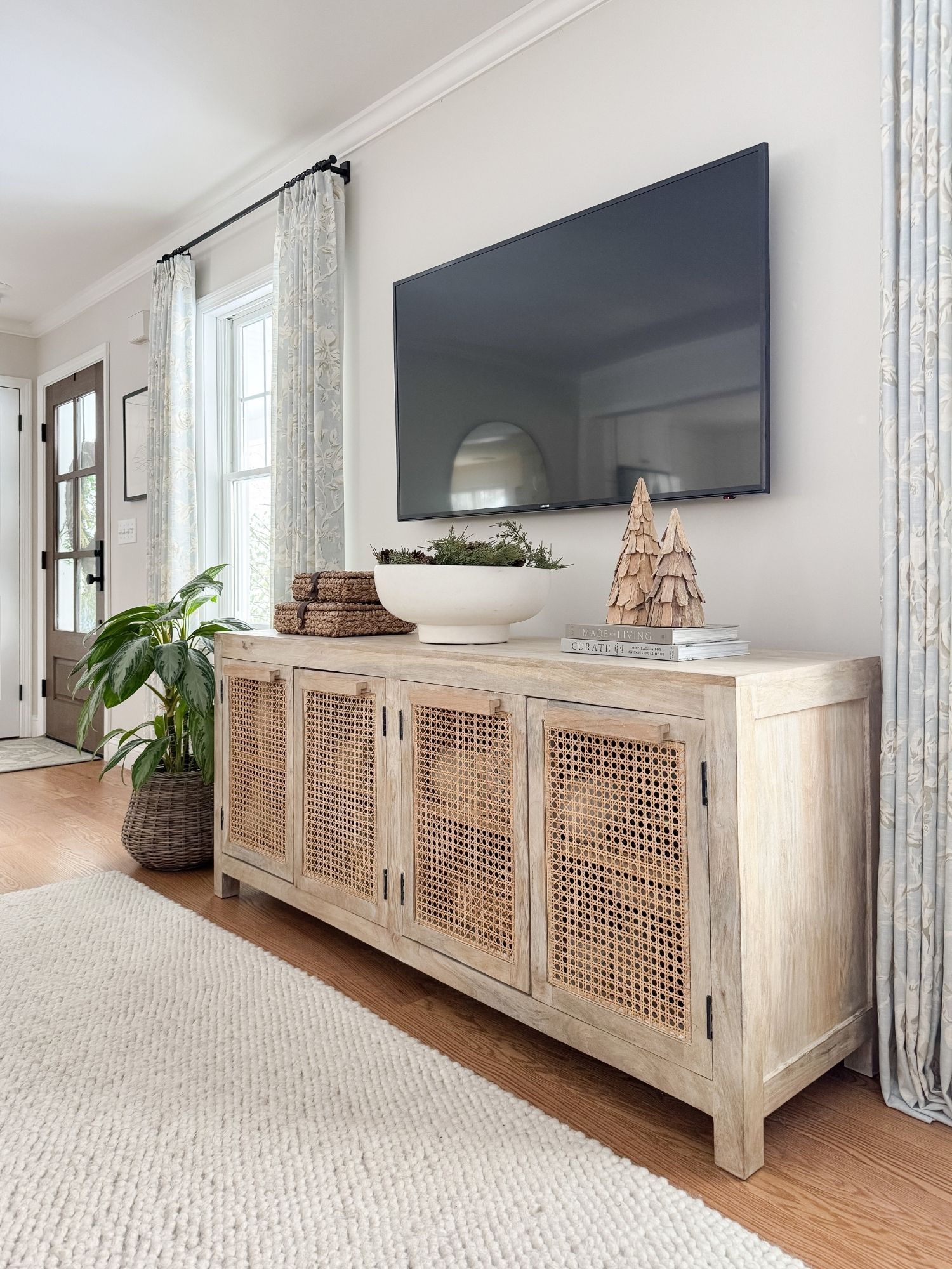 Family room storage cabinet with distressed wood and cane doors styled beneath a mounted TV for hidden storage and organization.