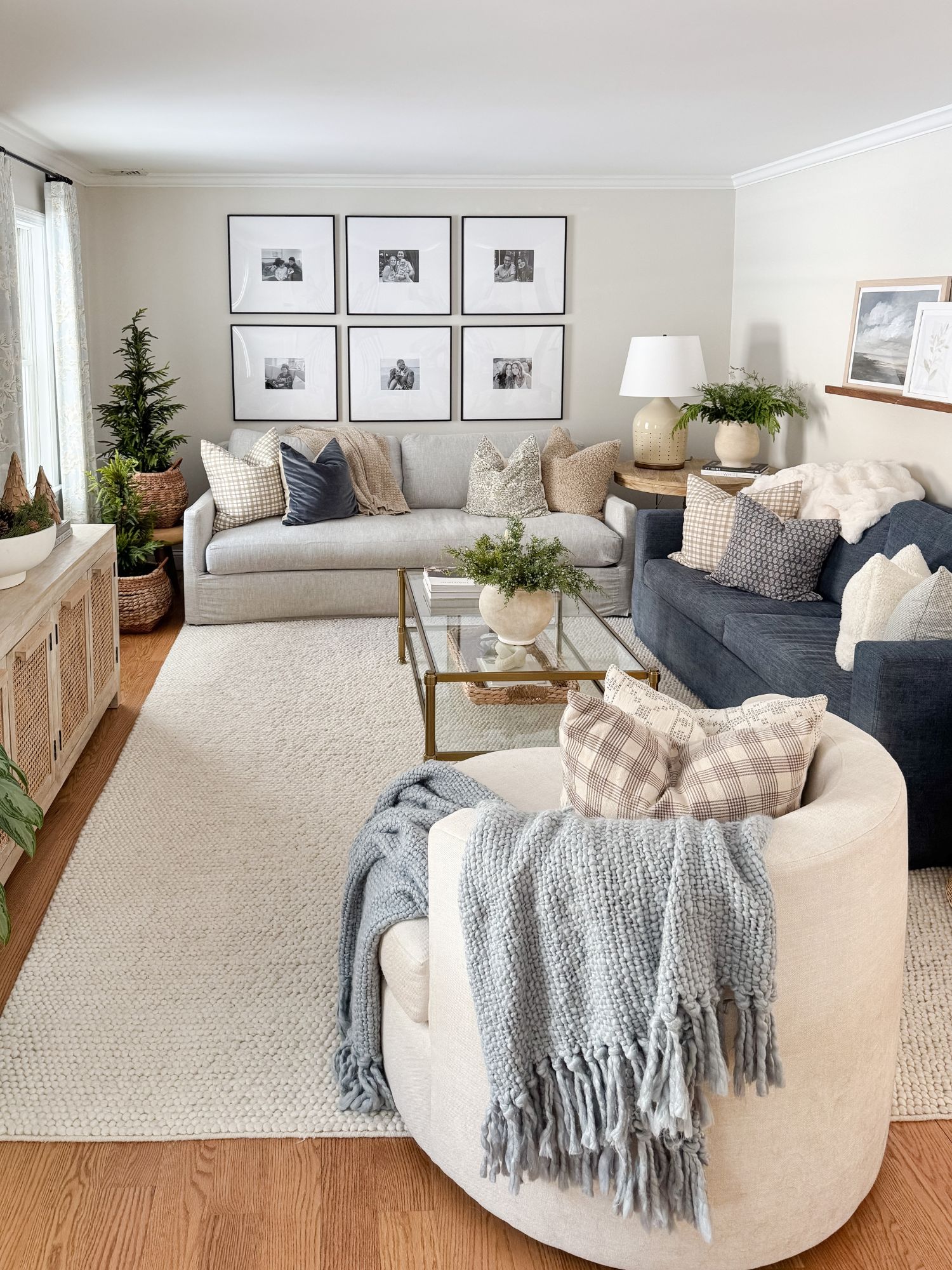 Cape Cod style living room featuring boucle storage ottomans, chunky knit throw blankets, neutral sofas, and subtle winter greenery for a cozy coastal feel.