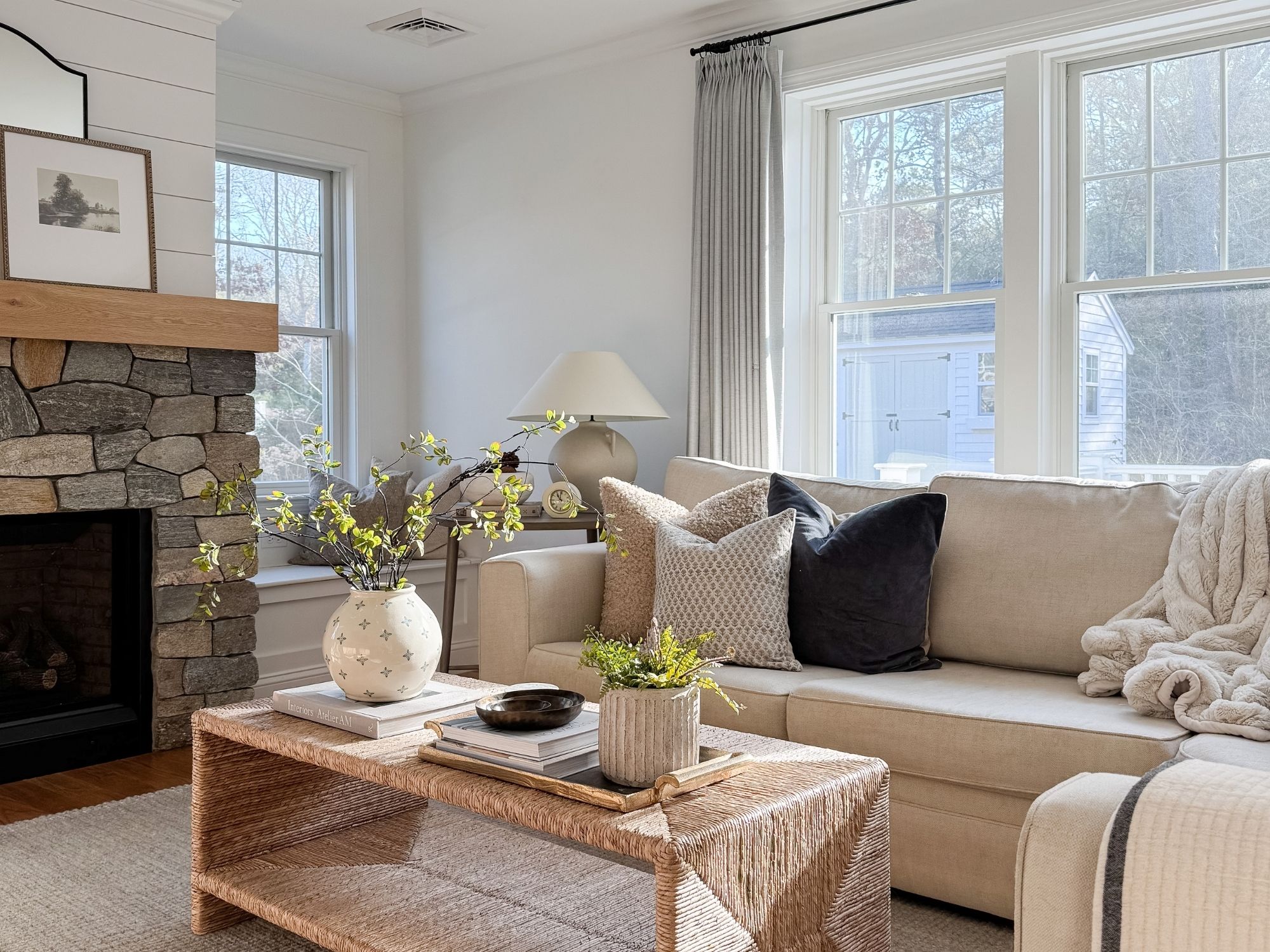 Cape Cod inspired winter living room with a neutral sofa, woven coffee table, ceramic vase, soft area rug, and white table lamp layered with natural textures.