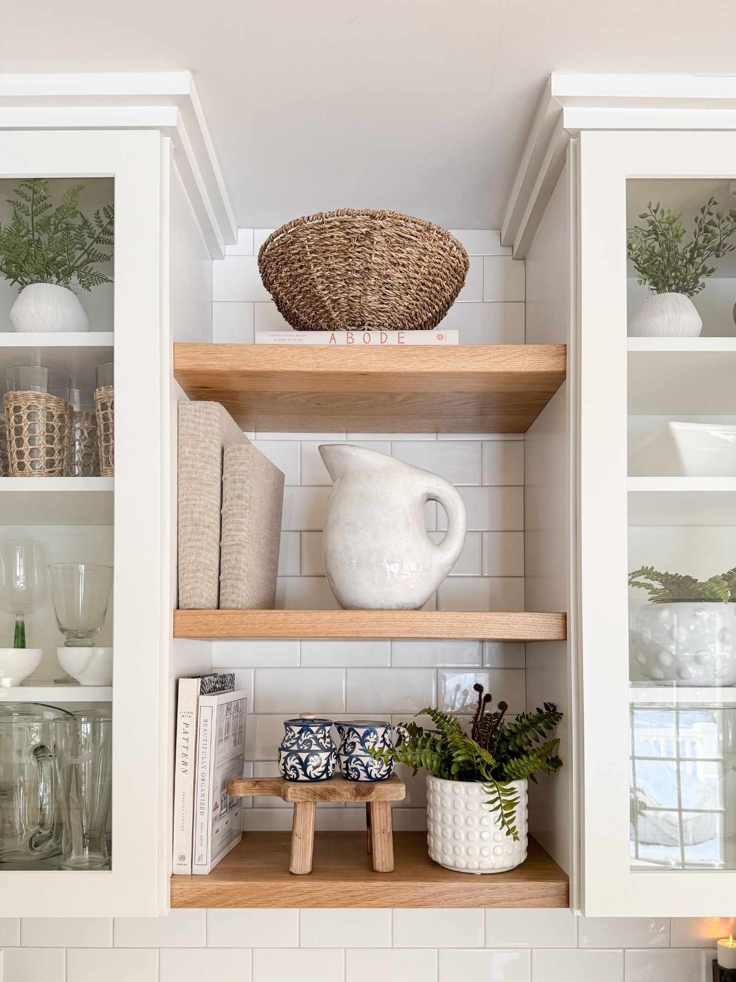 Neutral coastal kitchen shelves styled with white ceramic vases, greenery, wood textures, and relaxed Cape Cod inspired decor.