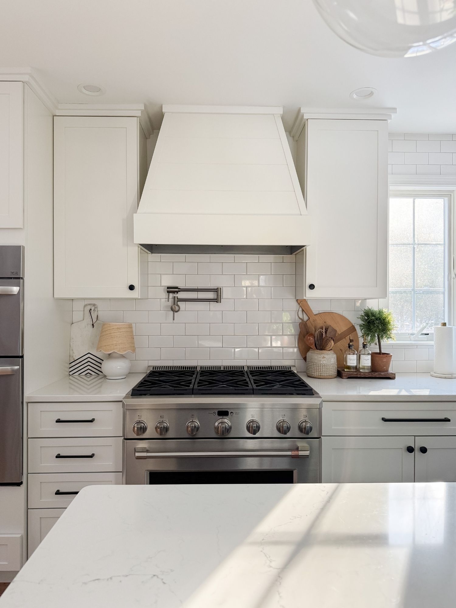 Coastal kitchen counter styling with natural wood serving boards, knife block, marble backsplash, and neutral Cape Cod inspired decor.