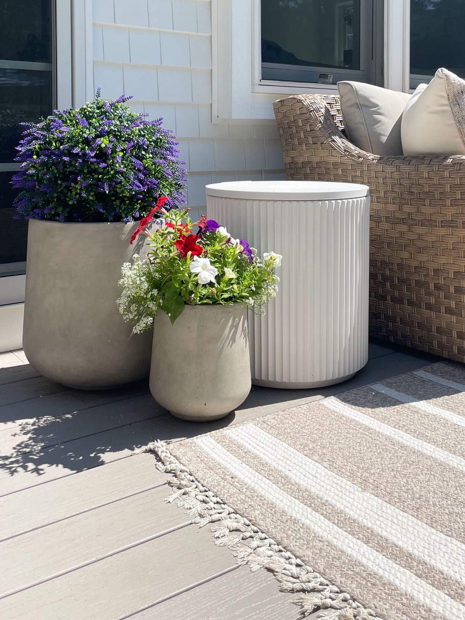 Coastal patio styling with neutral outdoor planters, artificial lavender plants, woven patio furniture, and striped outdoor rug for a coastal inspired patio.