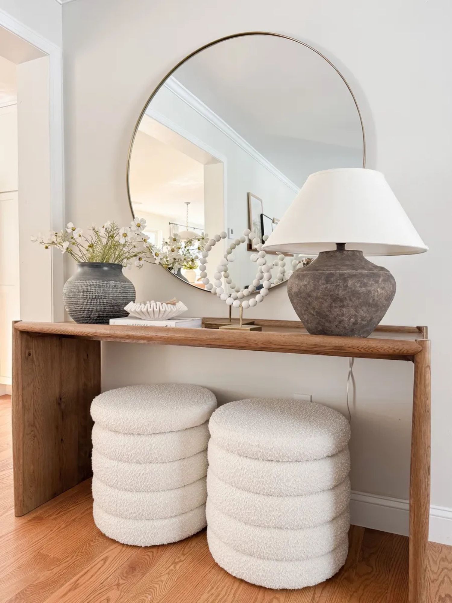 Coastal entryway styling with wood console table, boucle storage ottomans from Amazon, round mirror, faux cosmos flowers, and neutral decor in a light coastal home.